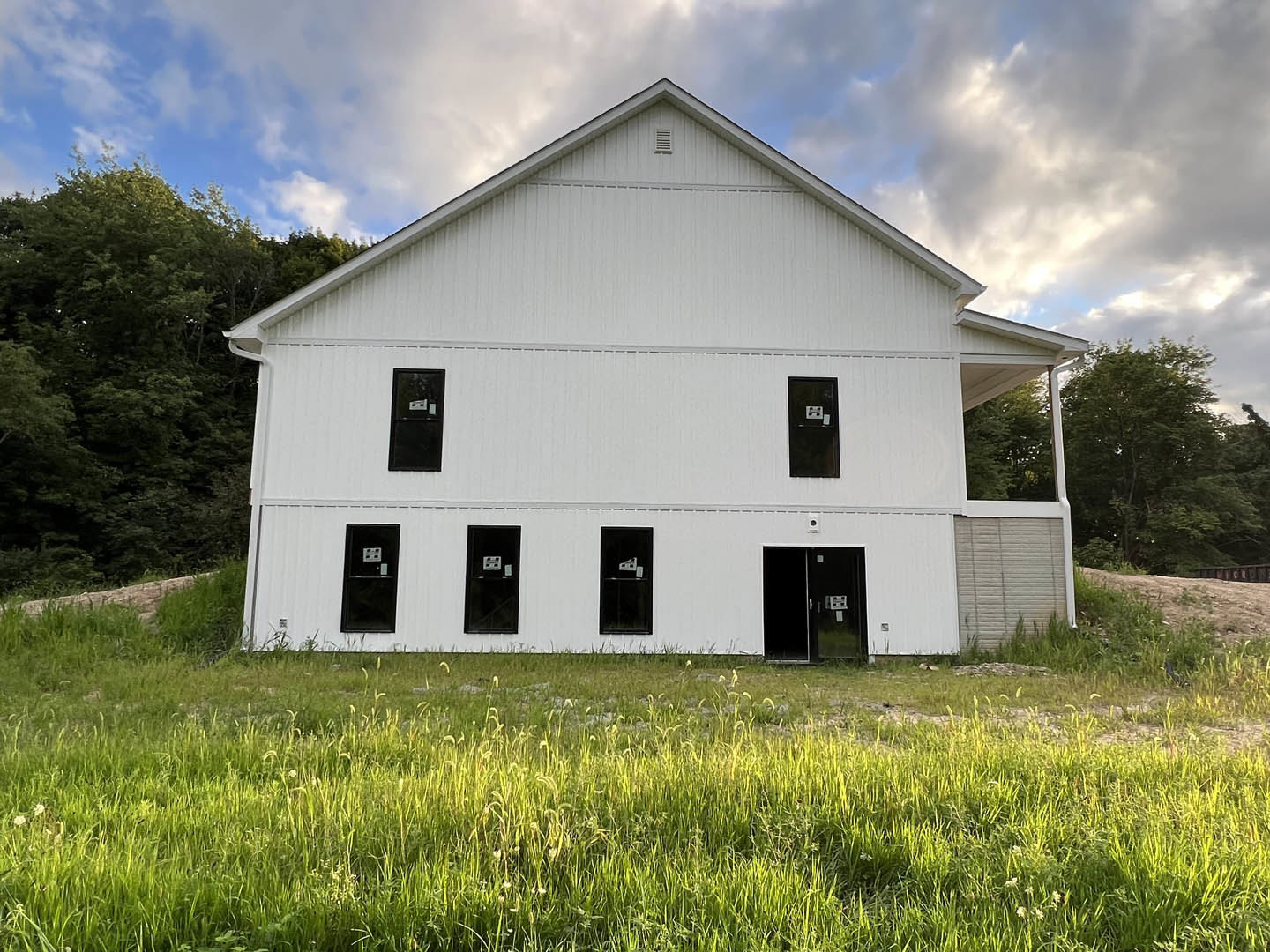 White farmhouse-style home with black-framed windows, glass doors, and white siding, set on a grassy lawn under a partly cloudy sky.
