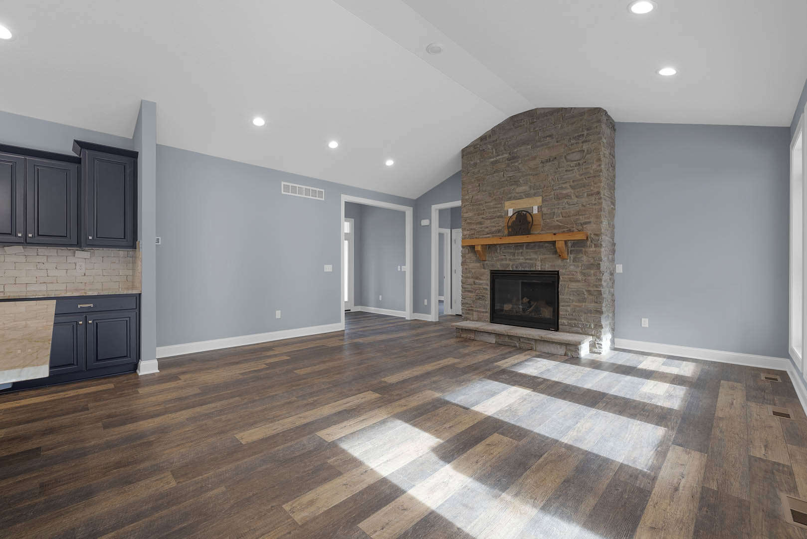 Living room featuring a stone fireplace with glass door, wood mantel shelf, hardwood flooring, white plaster ceiling with recessed lights, and black metal circular sculpture.