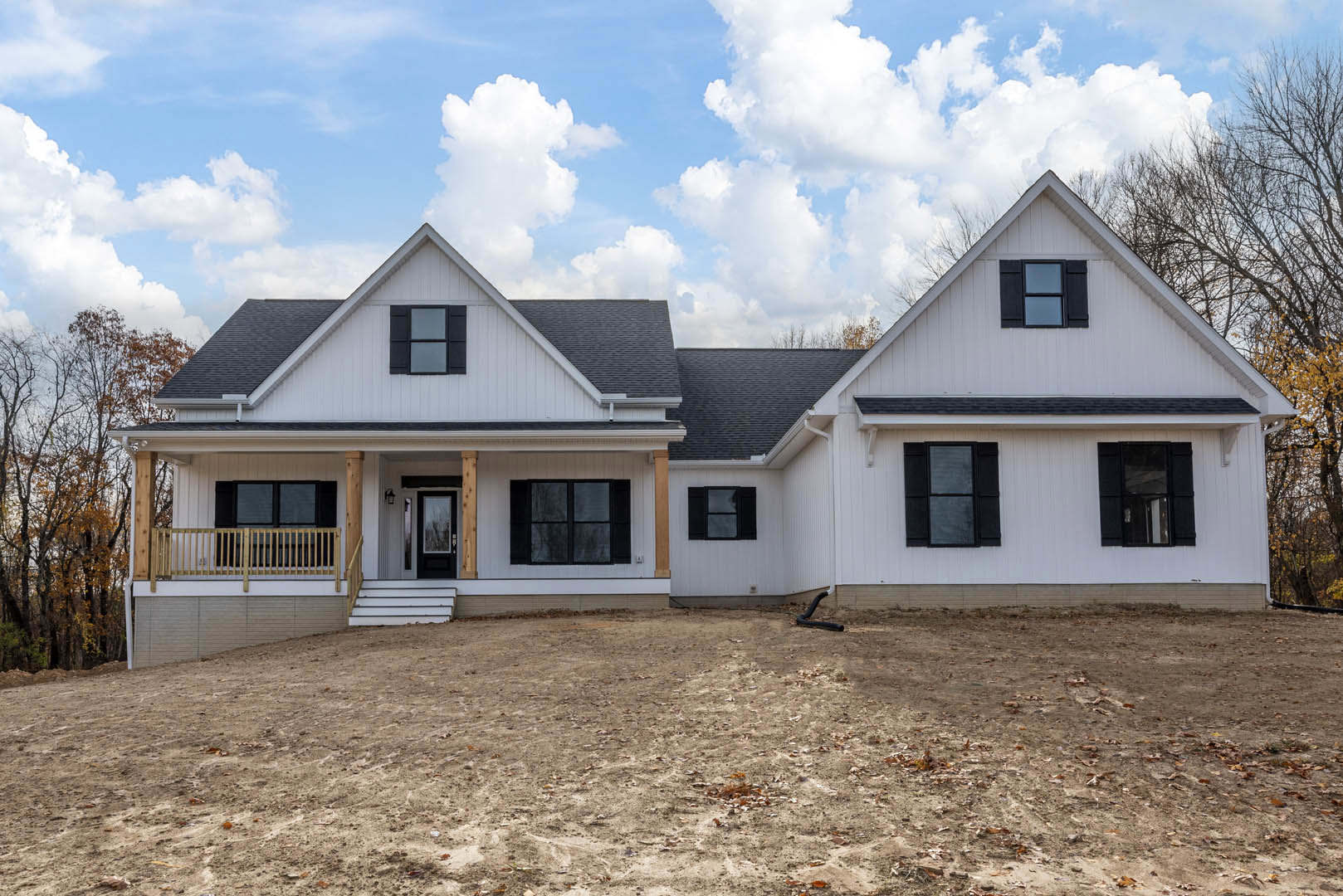Modern house with black-framed windows, large dirt yard, garden hose, and blue sky with scattered clouds