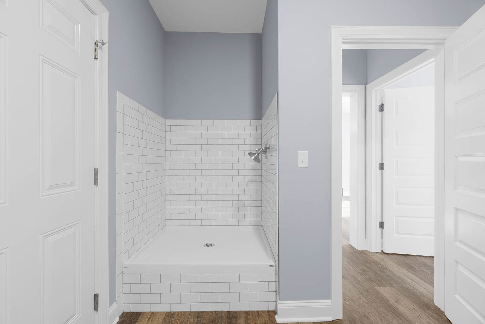 White tile shower with chrome showerhead, glass door, and plaster walls in modern bathroom