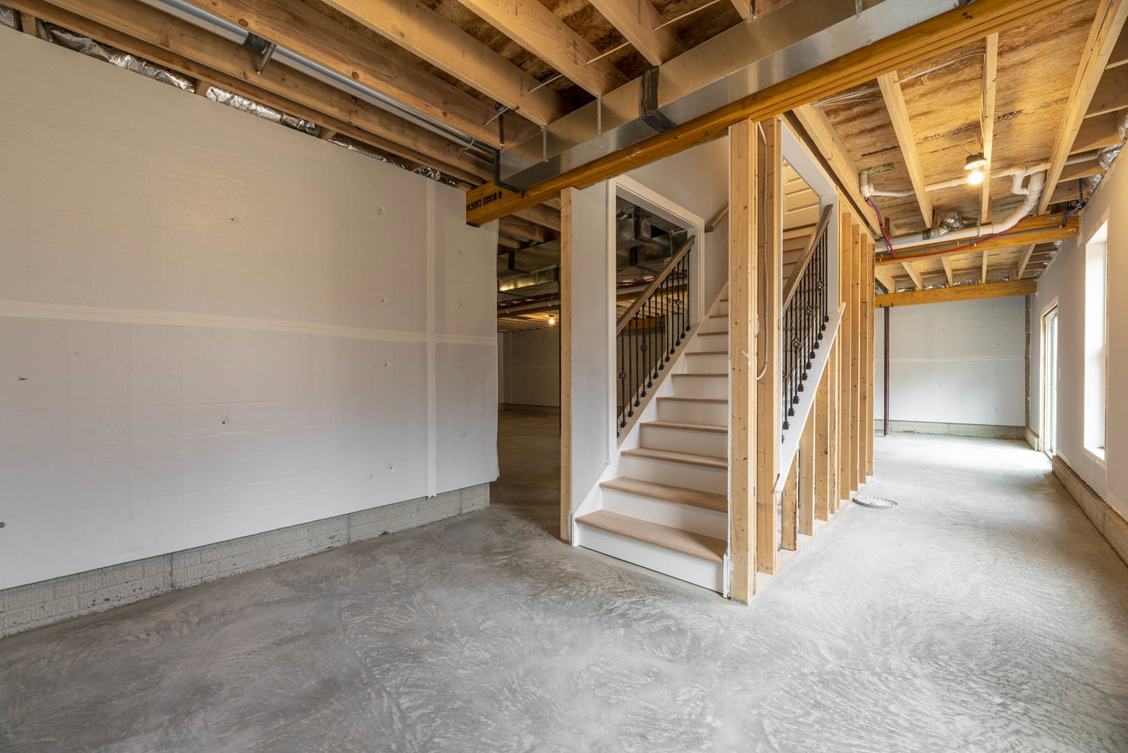 Open staircase with white and brown steps, concrete floor, exposed wooden ceiling beams, metal framing, and white plaster walls in a modern home interior