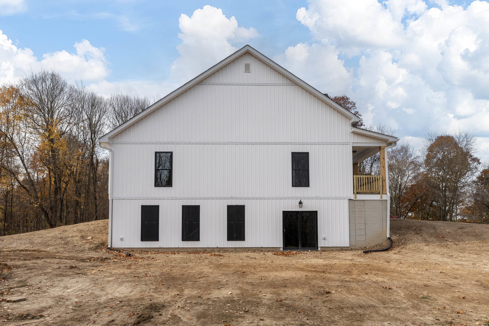 White house with black-framed windows and double doors, covered front porch, large yard with scattered leaves, and trees with yellow foliage.