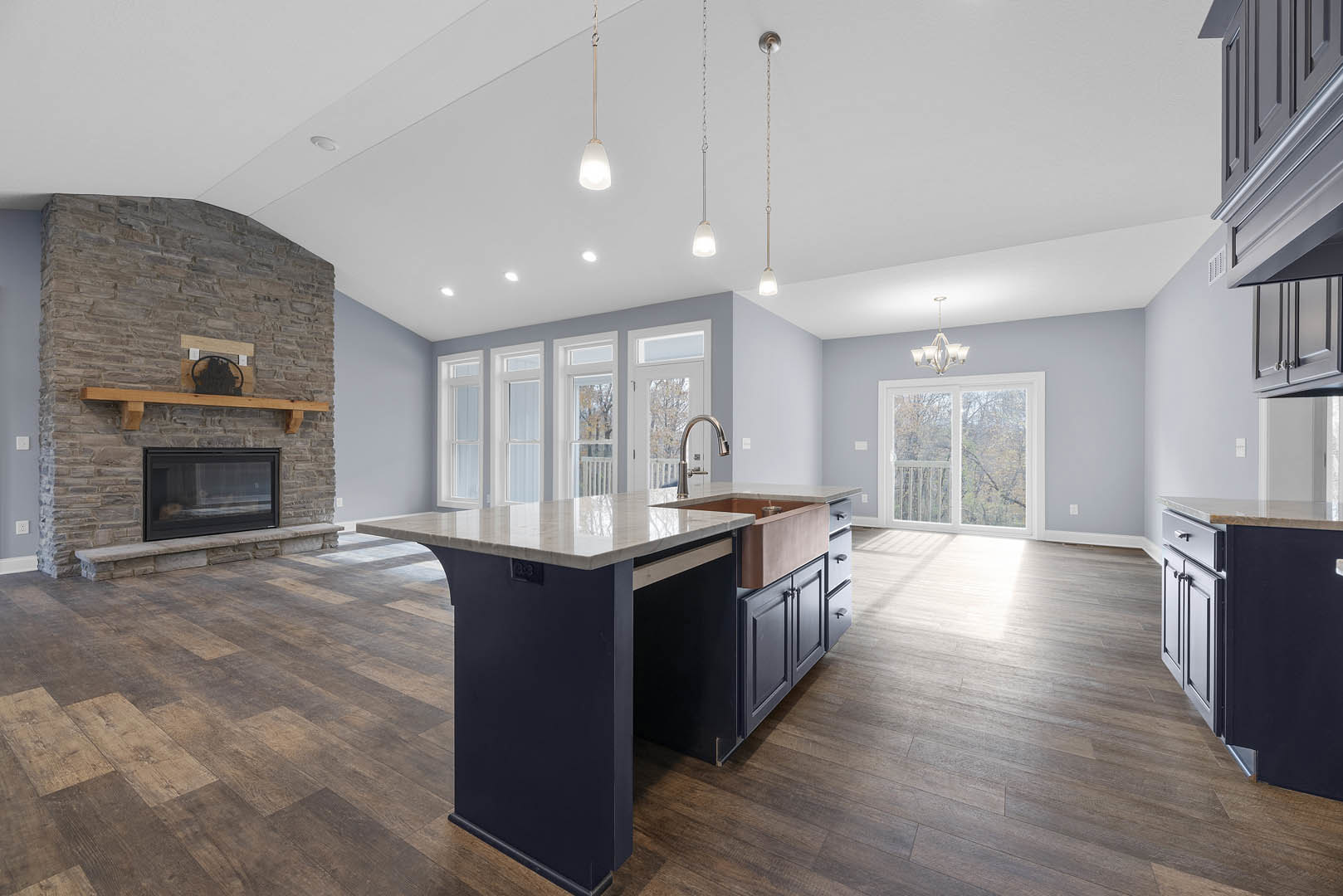 Spacious kitchen featuring a large island with built-in sink, white cabinetry, stone accent wall, modern fireplace with wood mantel, and sliding glass door.