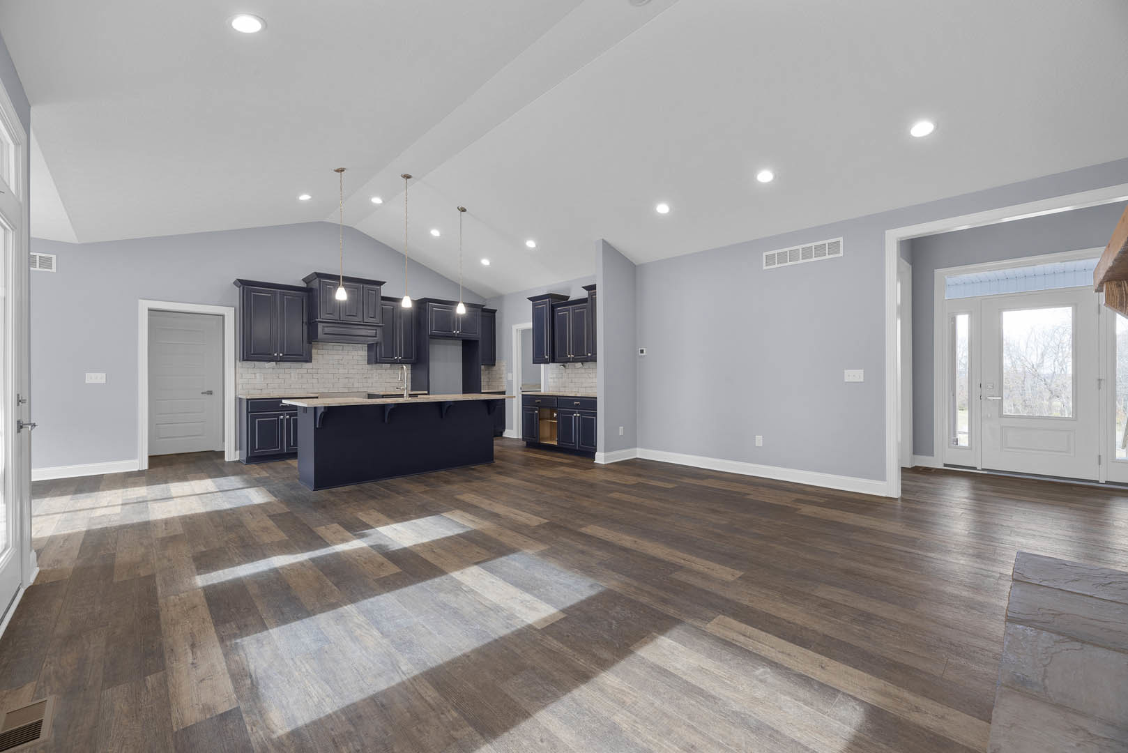 Spacious kitchen and dining area with wood flooring, black cabinets topped with white countertops, white doors including one with a window, and large windows offering a view of