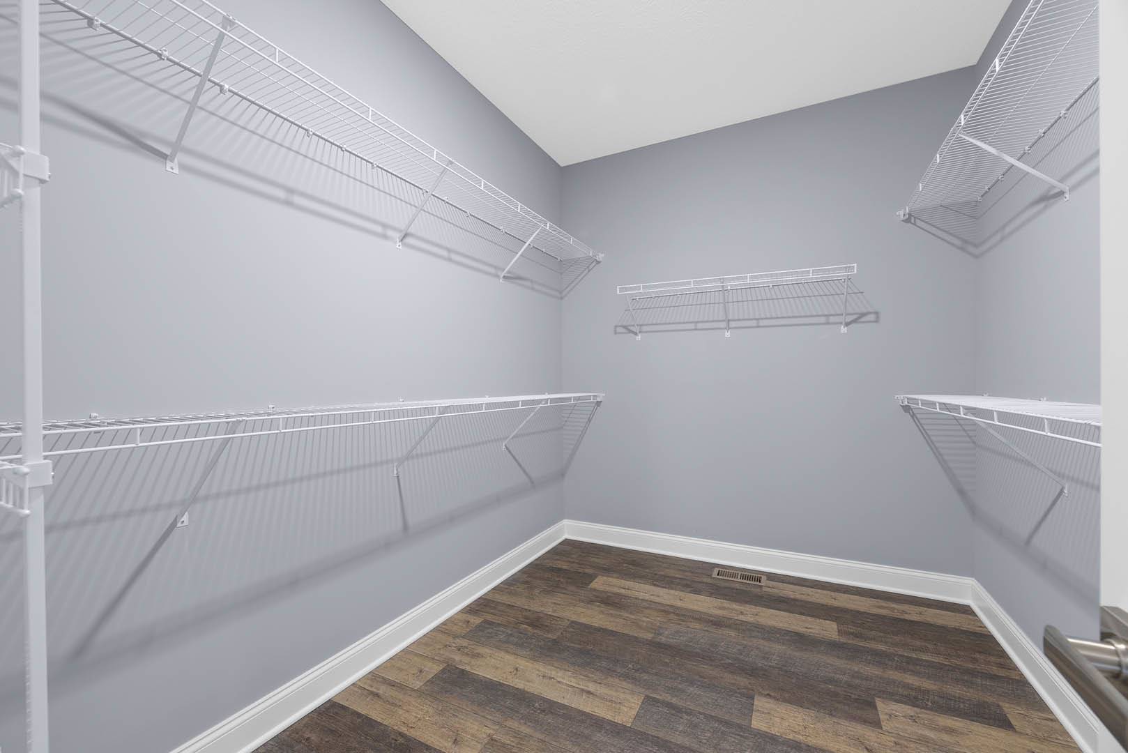 White built-in shelves against a plaster wall, wood floor with vent, white railing along stairs, white ceiling, rectangular shelf with black accent.