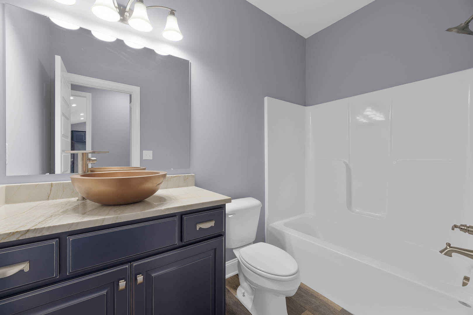 Modern bathroom with white ceramic sink, wall-mounted toilet, glass-enclosed shower, gray tile flooring, and light wood vanity with stone countertop