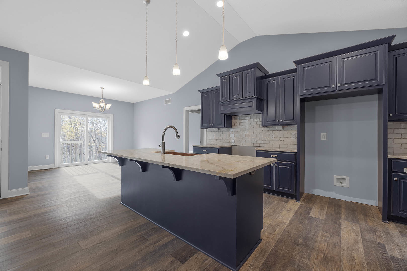 Spacious kitchen featuring a large marble-topped island, white cabinetry, stainless steel faucet, chandelier with white shades, sliding glass door, and light wood flooring