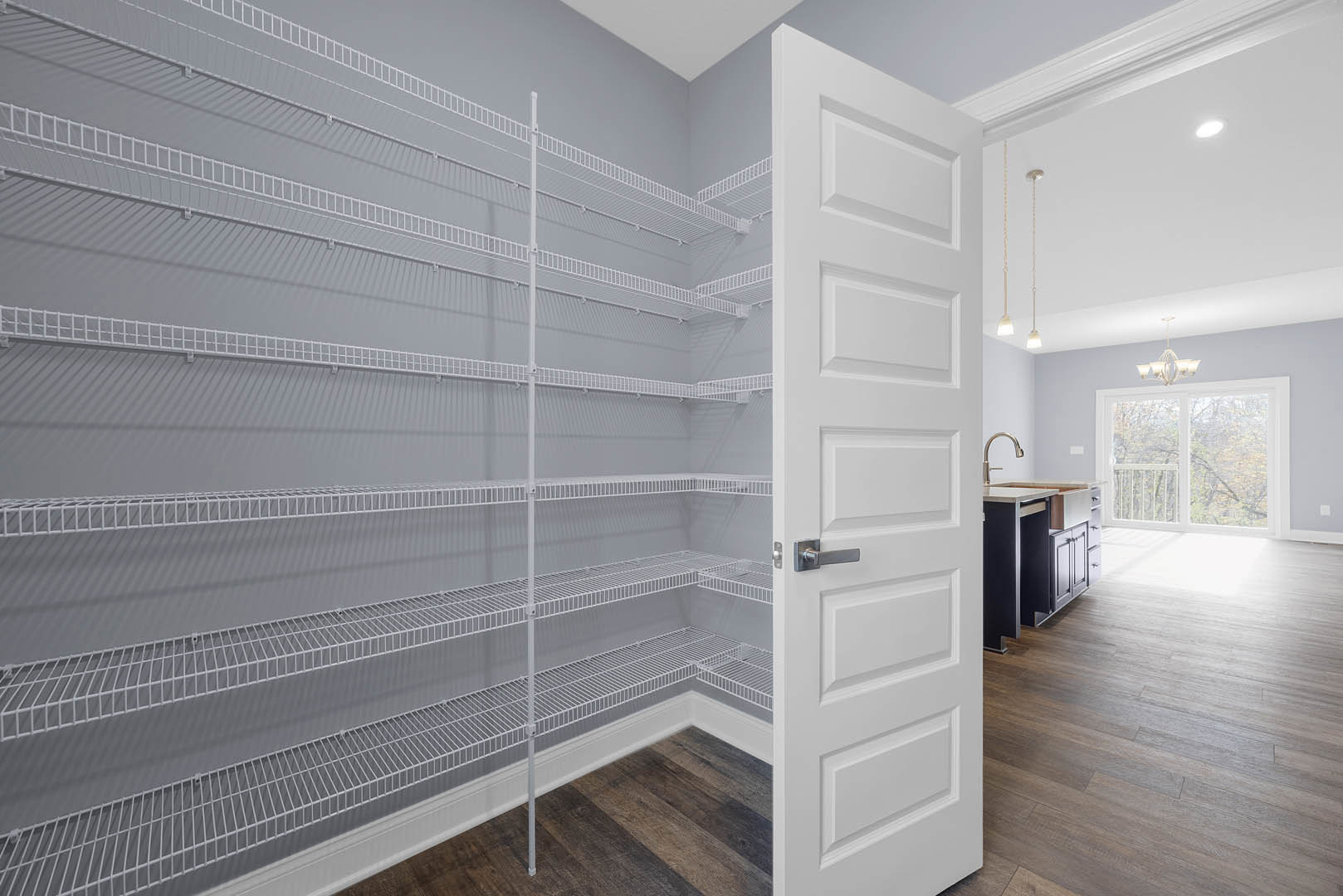 White door open to a room with built-in shelves, wood flooring, and plaster walls; window with balcony visible in background, kitchen area with white countertop and modern faucet.