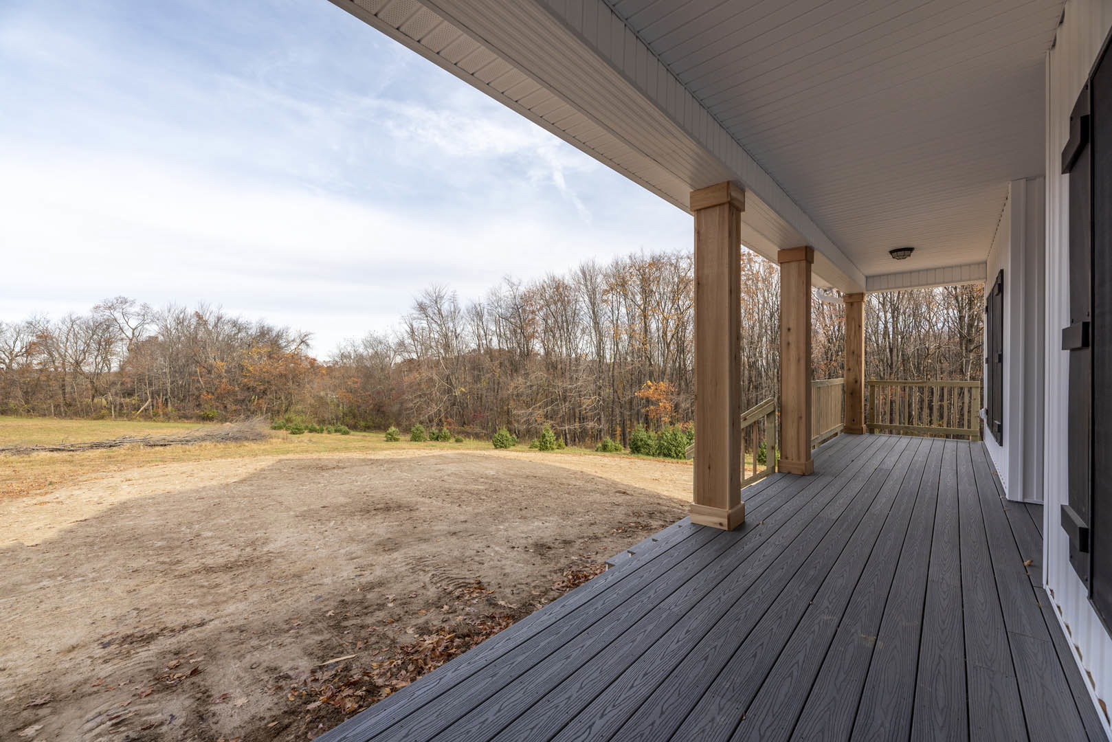 Wooden deck with railing overlooking dirt field, trees, and wooden fence in the background