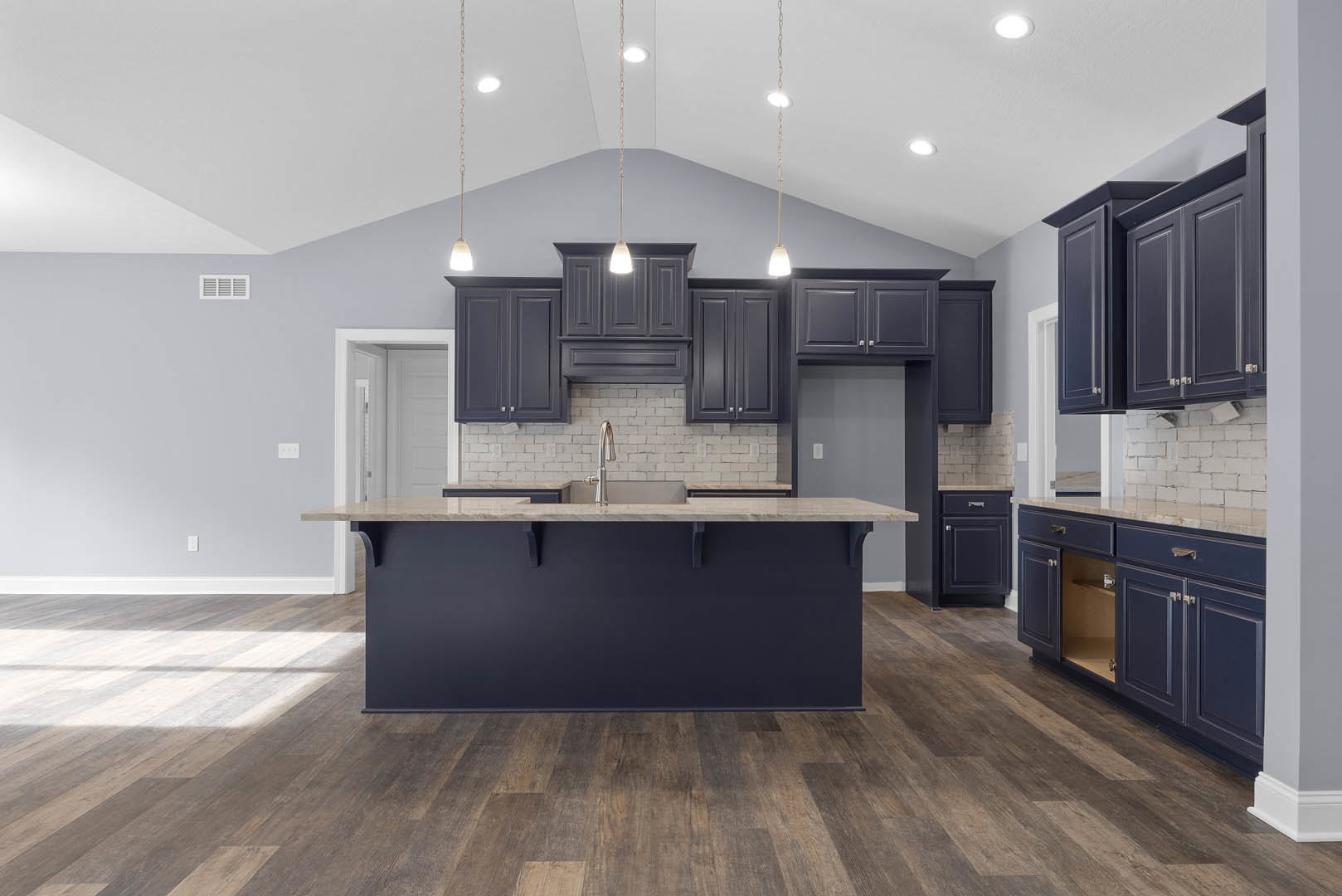 Spacious kitchen featuring a large central island with stone countertop and built-in sink, wood flooring, blue accent wall, white cabinetry, and stainless steel appliances