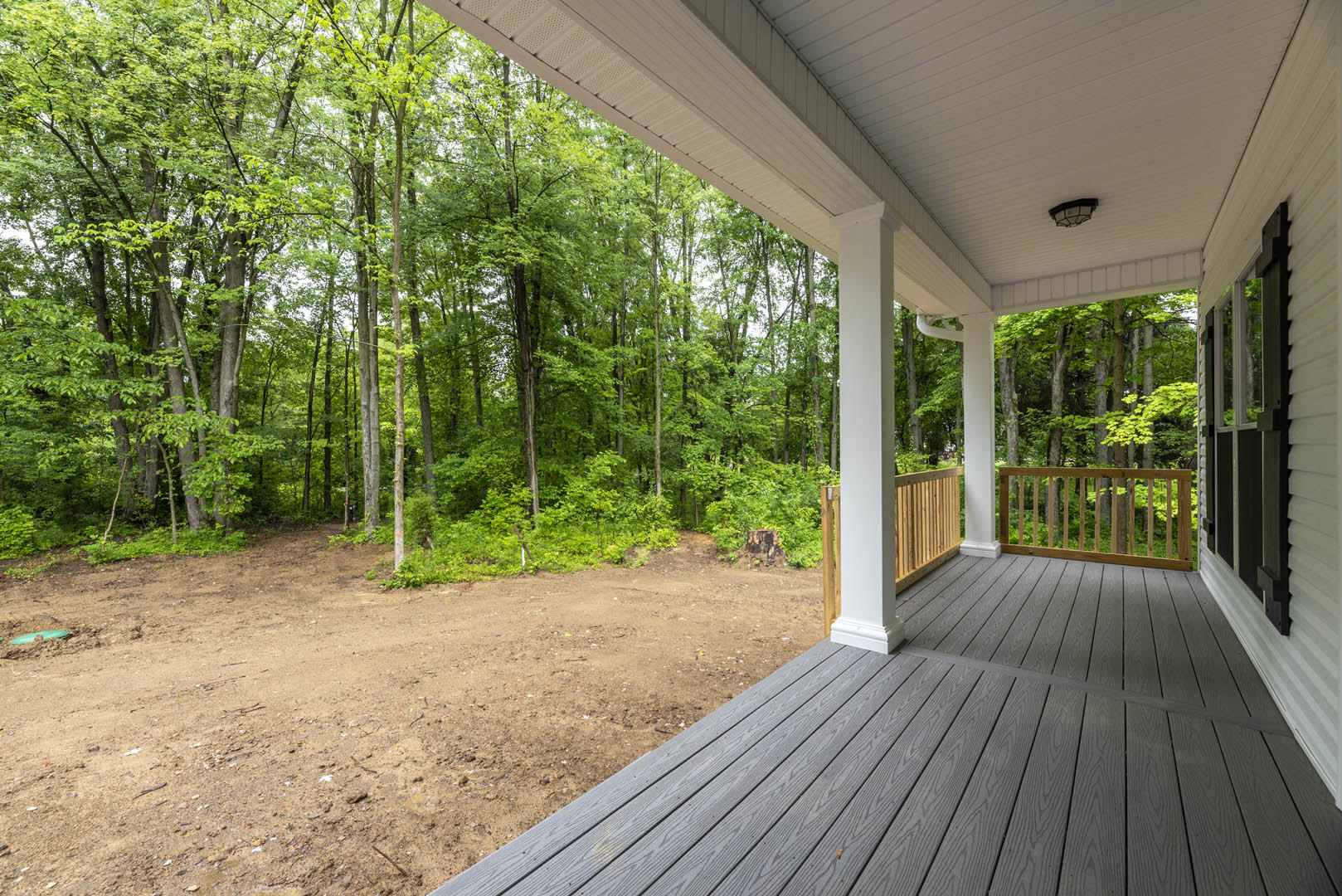 Wood porch with horizontal railing, surrounded by trees and a dirt path leading through the wooded landscape in the background