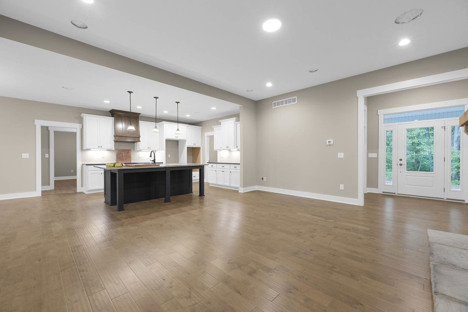 Spacious kitchen featuring a central island with stone countertop, white cabinetry, stainless steel sink, hardwood flooring, and a glass-paneled door.