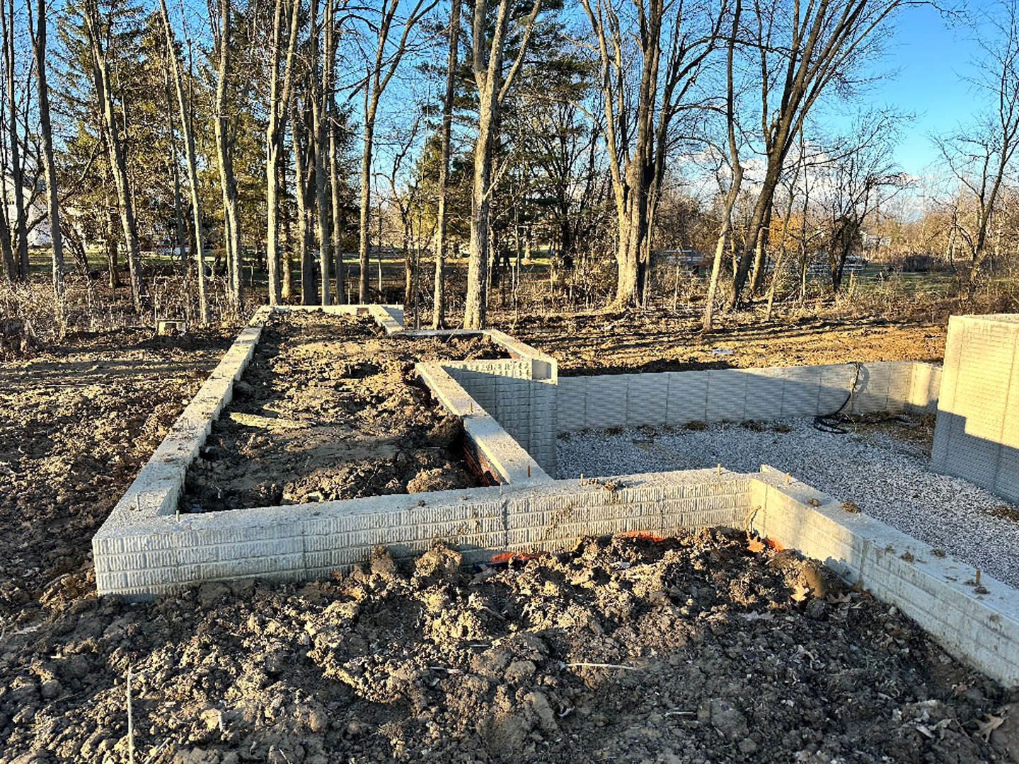 Concrete foundation slab surrounded by exposed dirt, with mature trees and forested background
