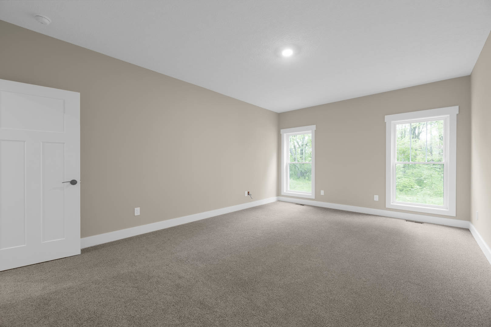 Carpeted room with large windows, white door, plaster walls, and view of trees outside