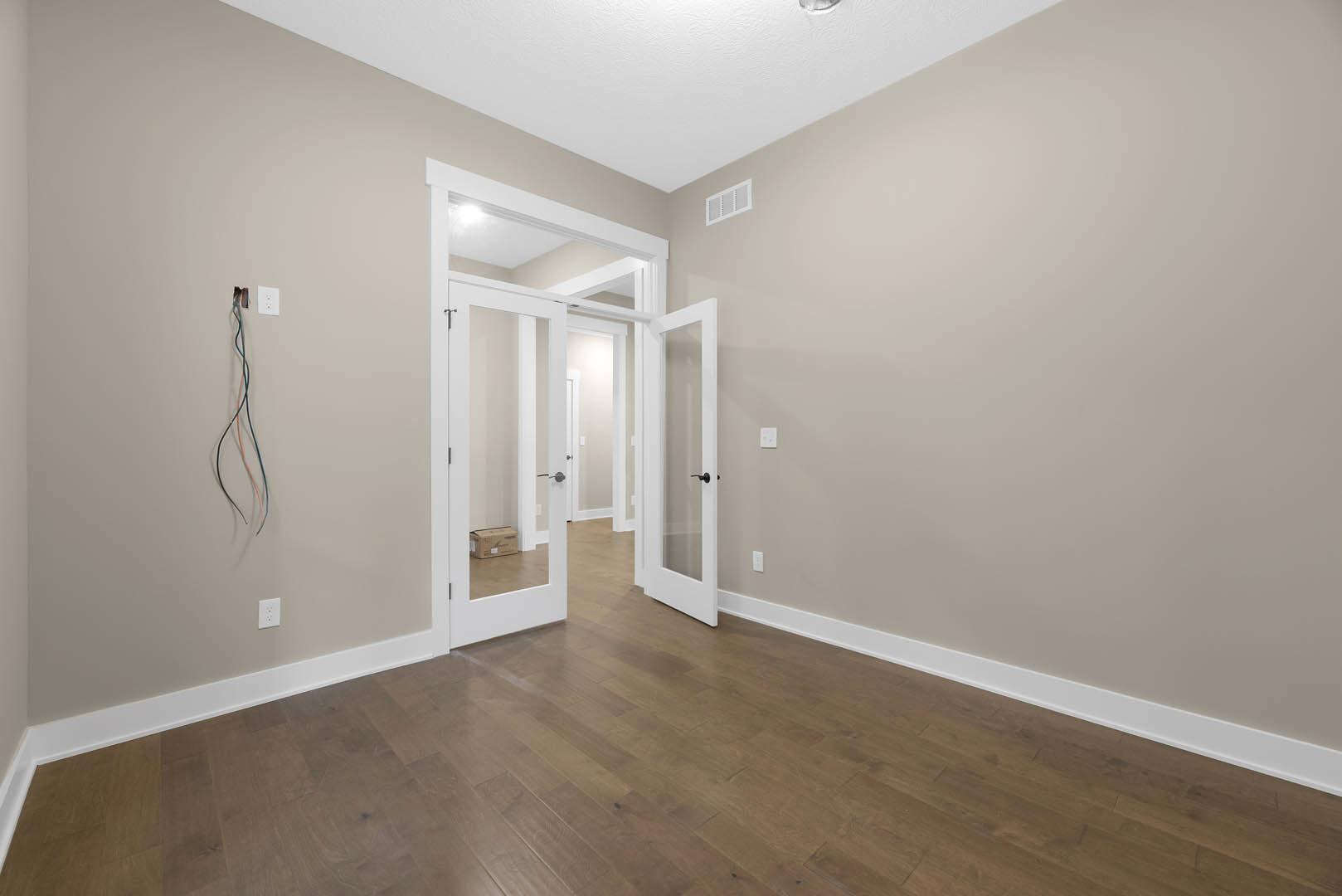 Wood flooring with white paneled doors, white wall vent, visible wall wiring, and plaster walls with molding