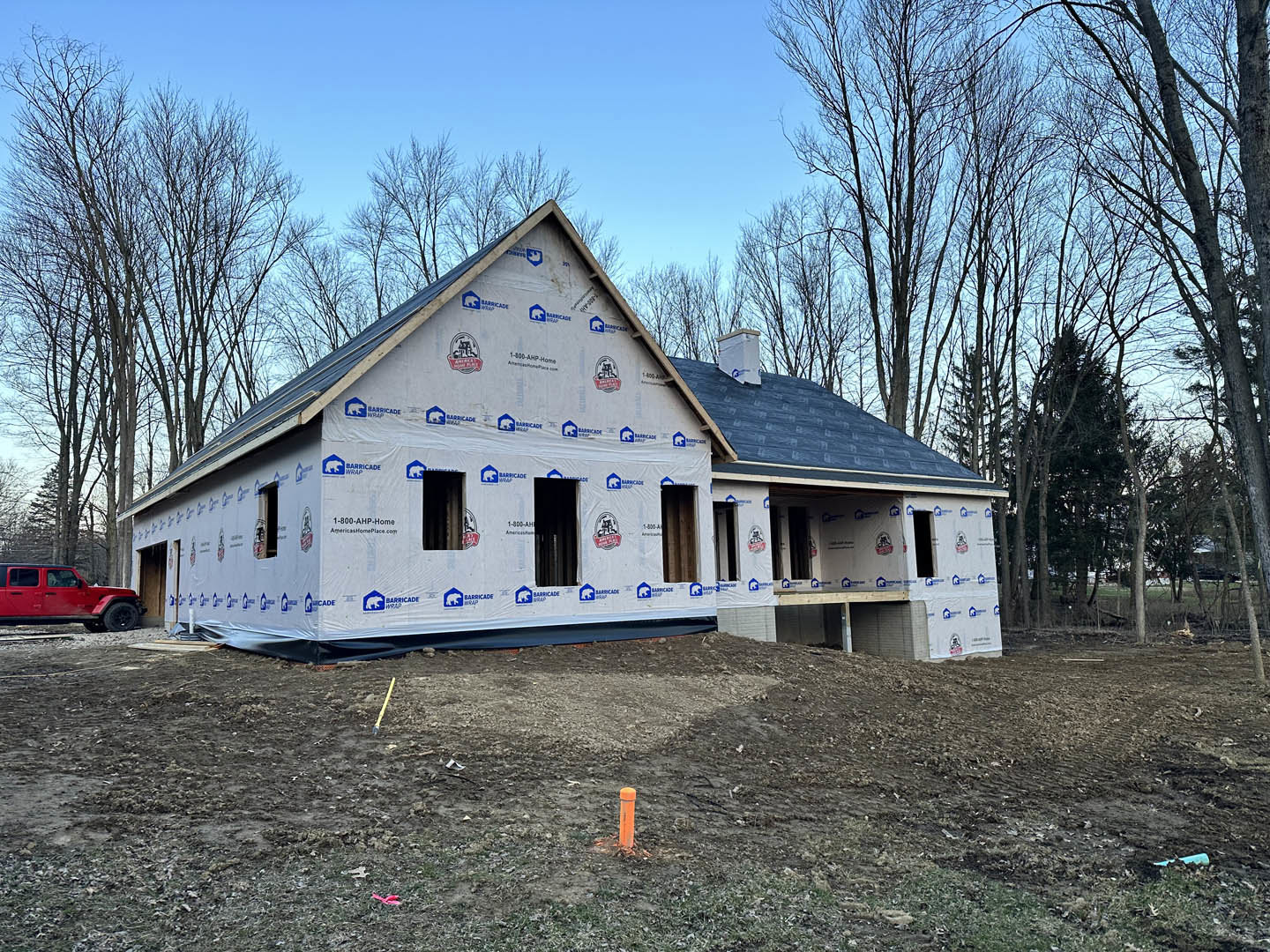 Framed house under construction with exposed wood panels, partially finished roof, and surrounding trees in the background