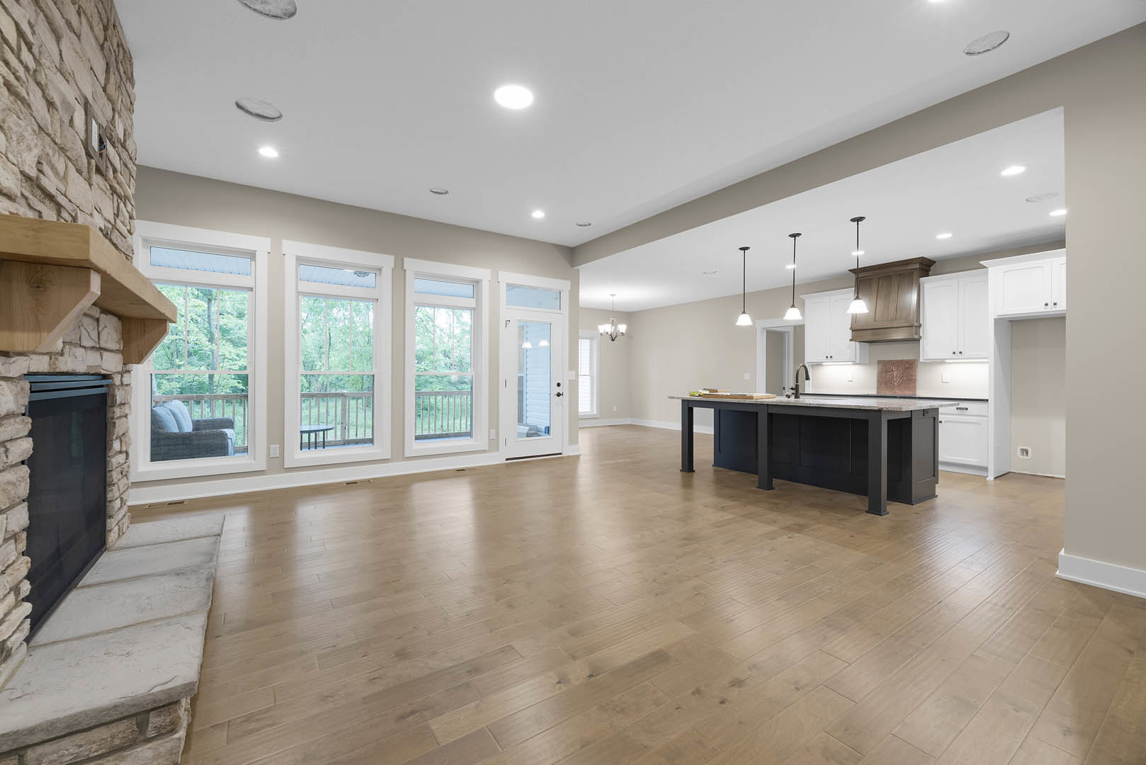Spacious kitchen and dining area with wood flooring, central island featuring a sink, stone accent wall with window, white cabinetry, and modern lighting