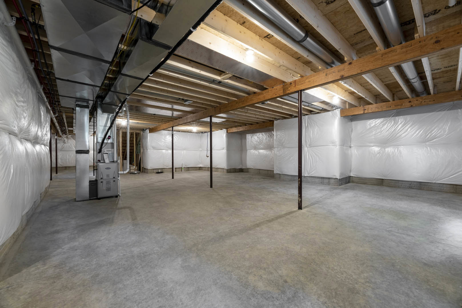 Concrete floor and white walls in an empty room, white plastic coverings draped along the wall and scattered on the ground, exposed ceiling beams visible overhead.