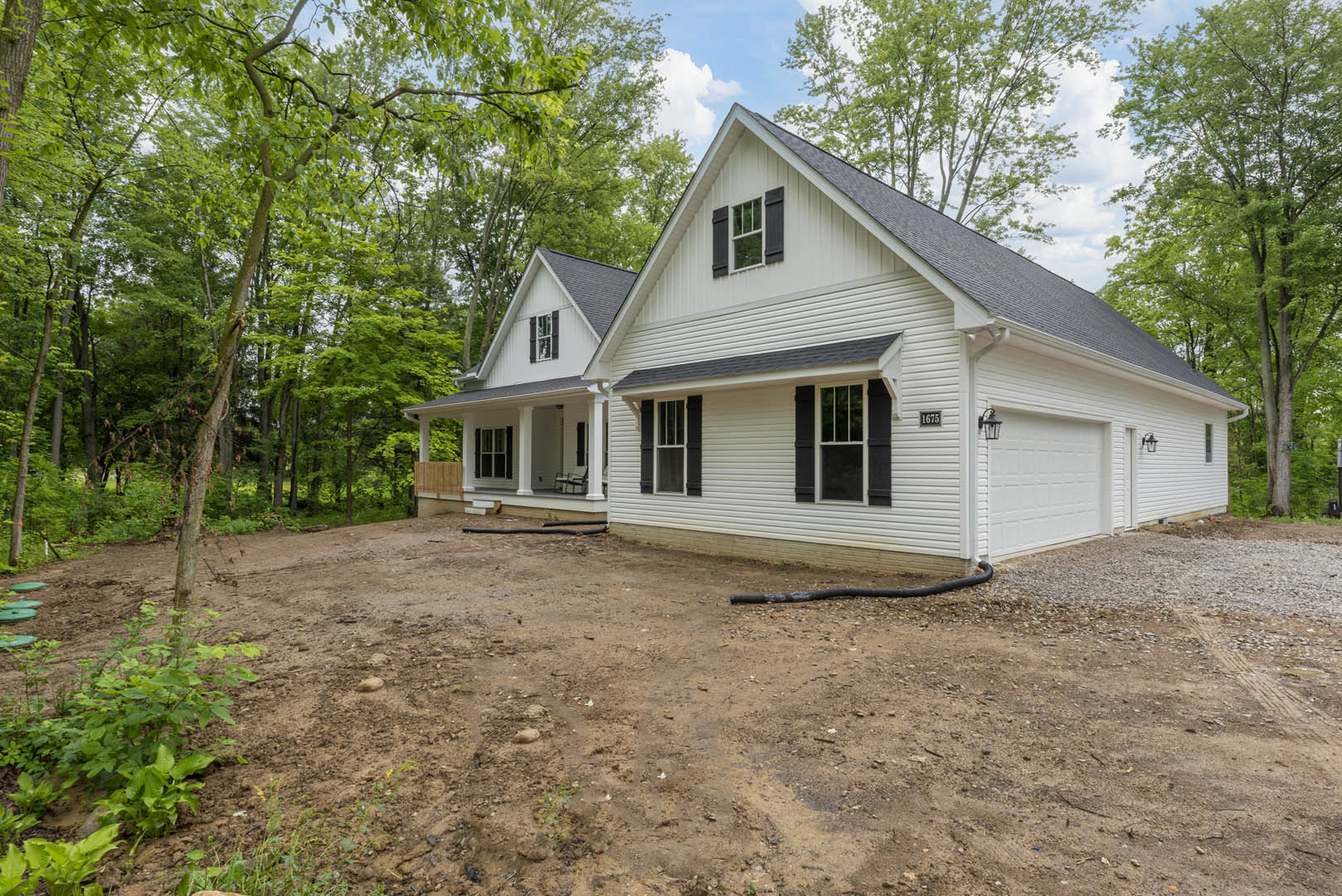 Two-story home with white siding, attached garage, paved driveway, mature trees, and wooden fence along landscaped yard