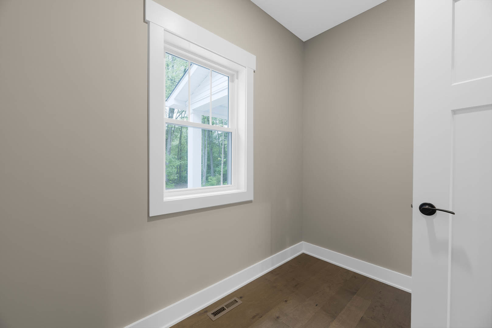 Bright room with white-framed window, light wood flooring, floor vent, white plaster walls, and ceiling molding