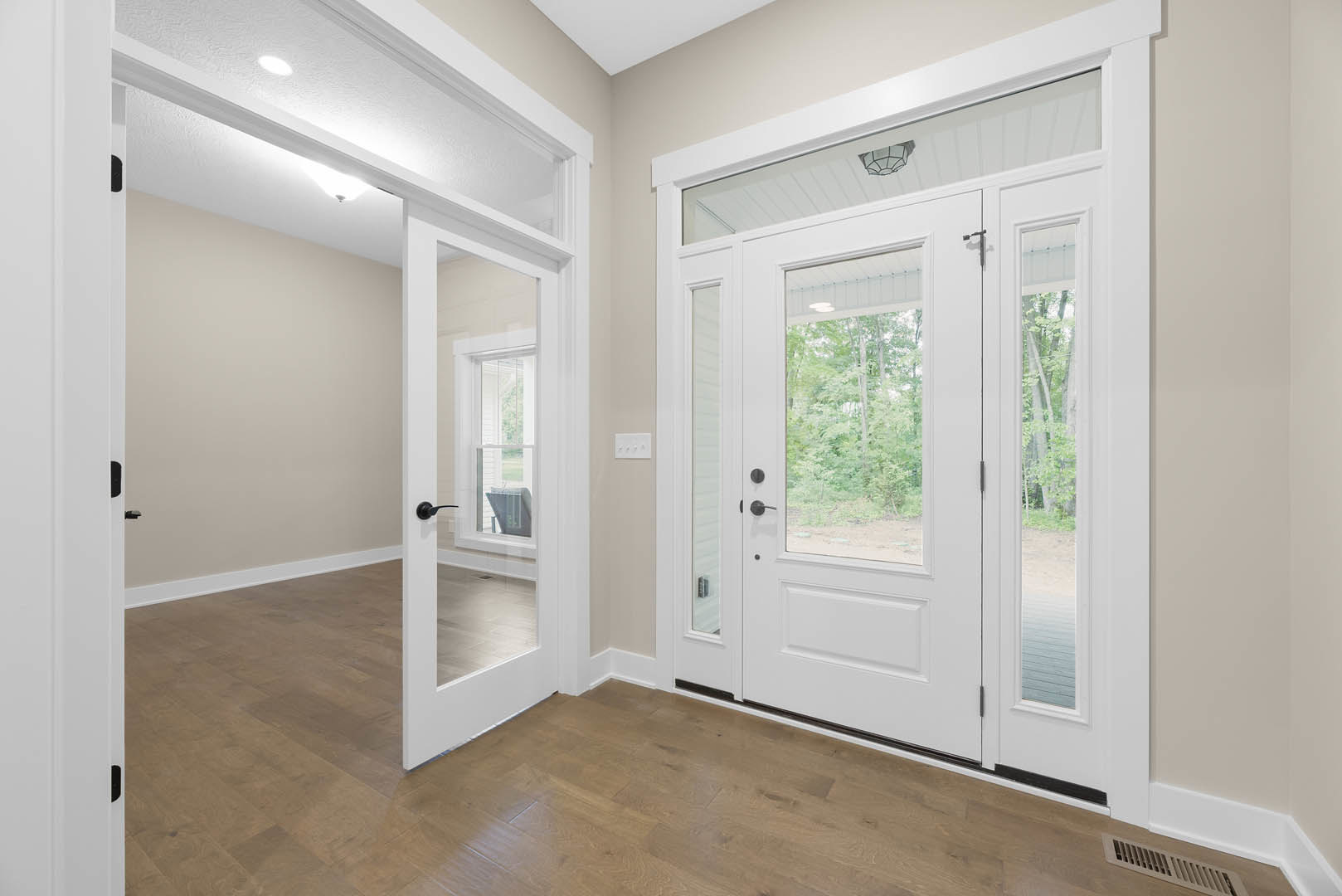White door with glass panes, wooden floor, glass-shaded light fixture, window showing trees outside, white walls with molding