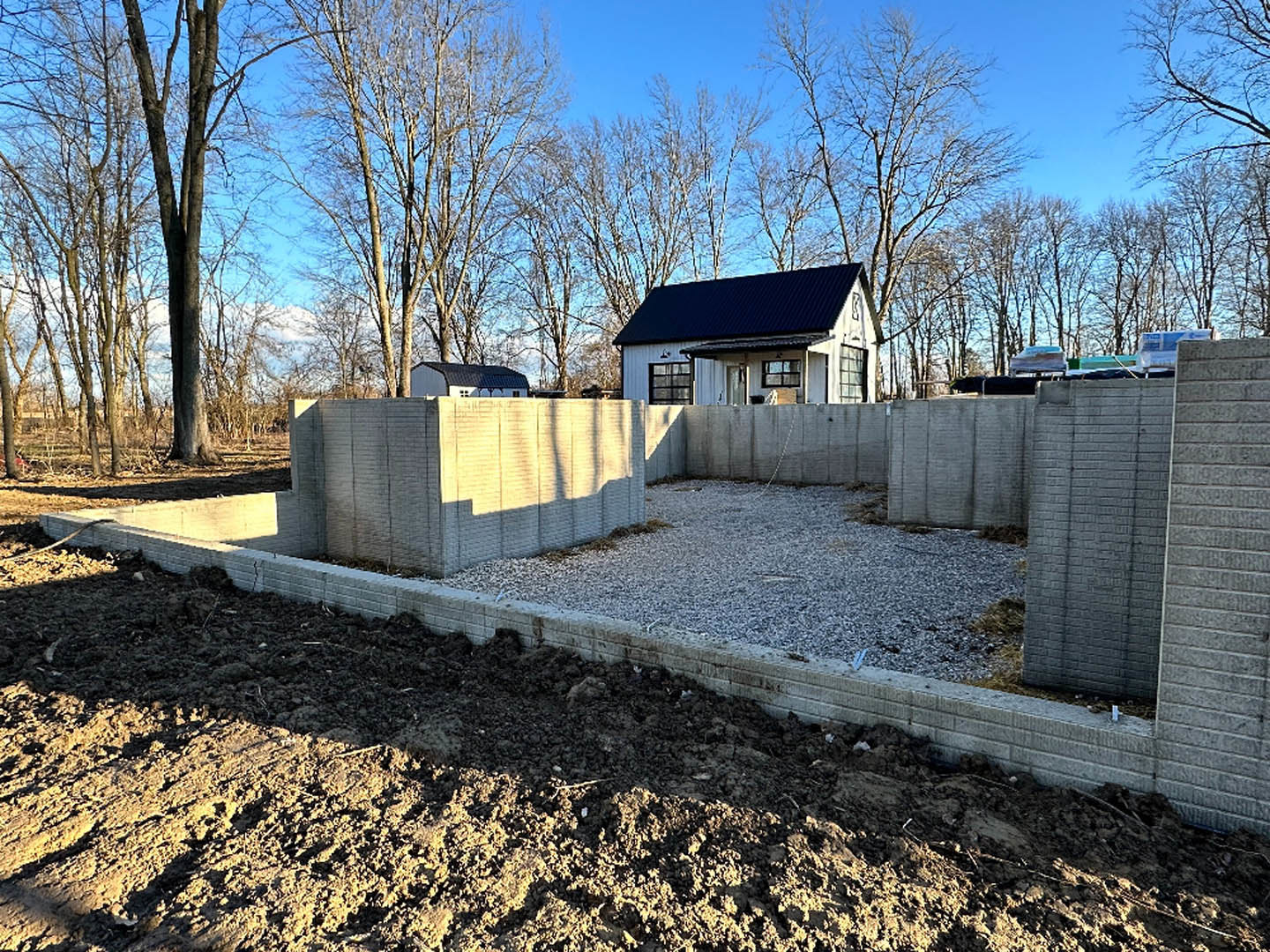 White house with black roof behind concrete and brick walls, surrounded by bare trees and winter landscape.