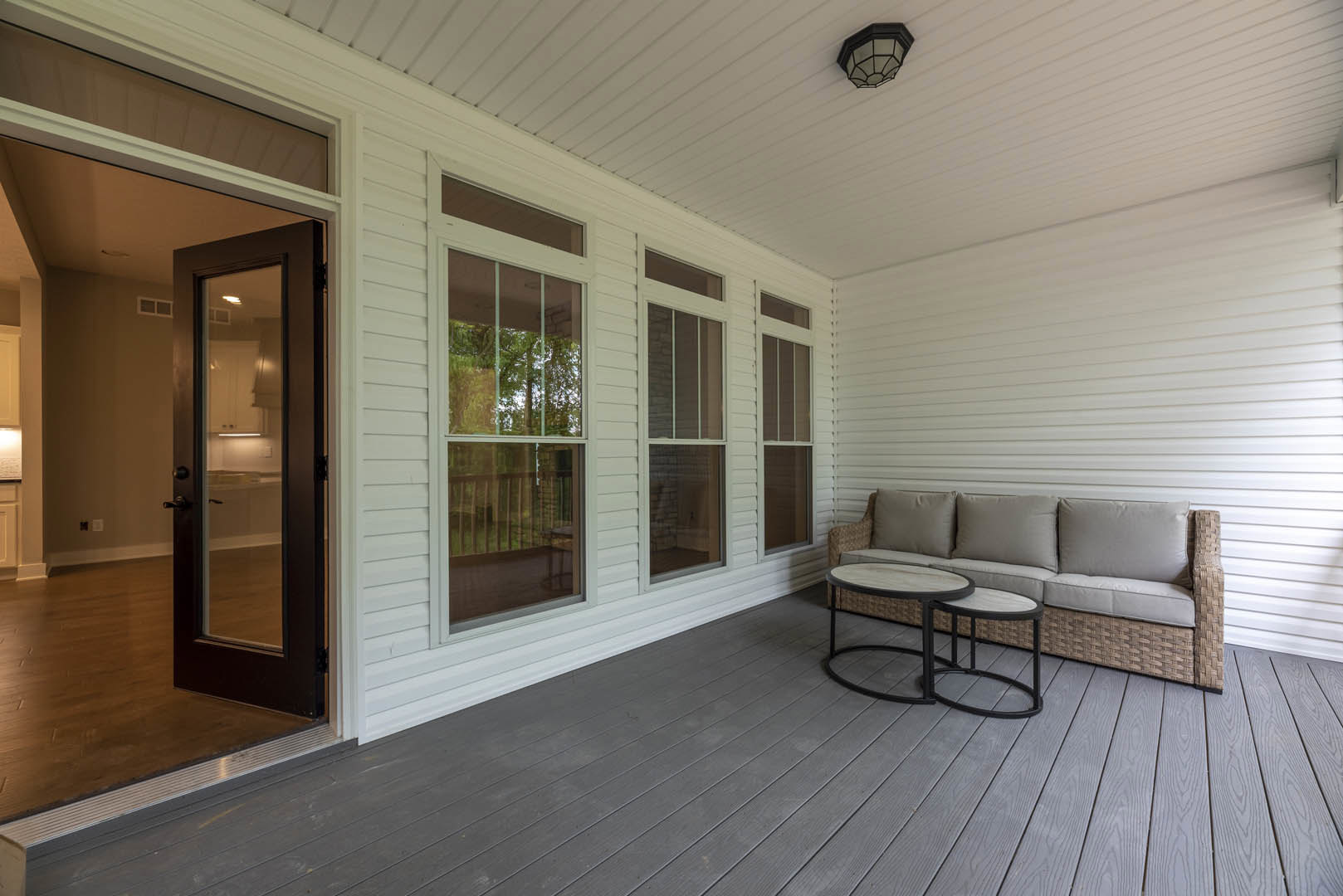 White-walled living area featuring a light gray couch and wooden coffee table, glass door revealing modern kitchen, large window with multiple glass panes, close-up of recessed