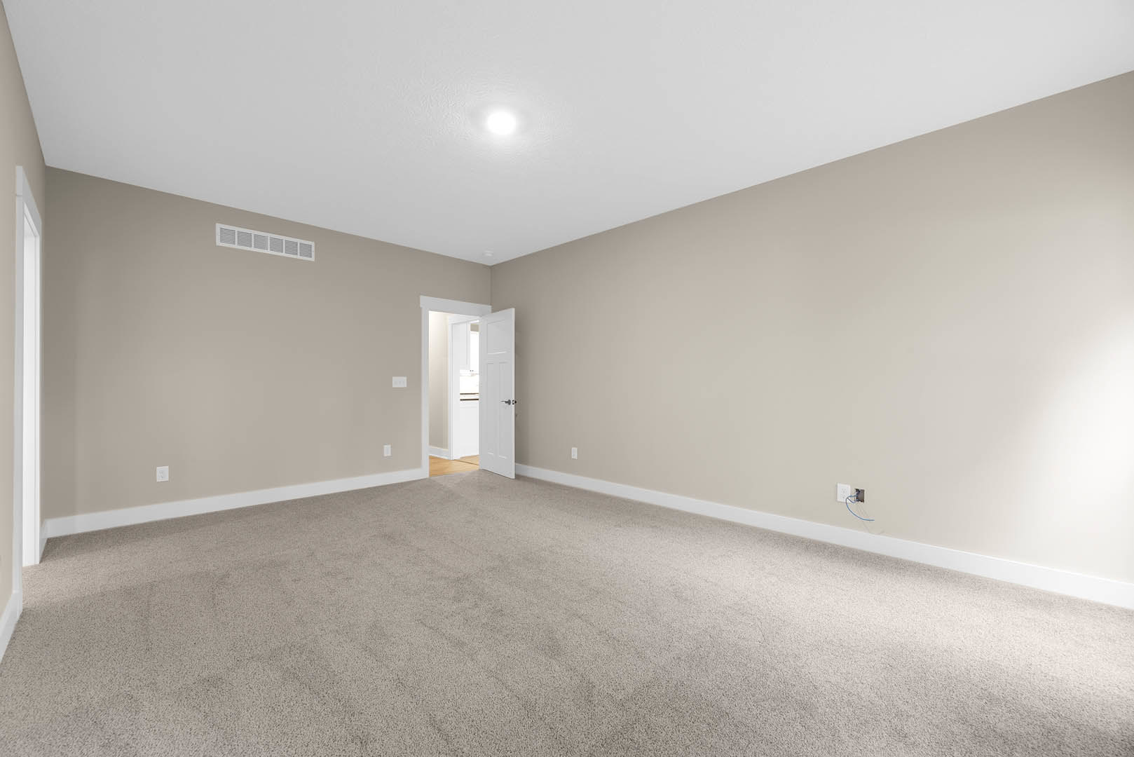 Carpeted room with white door open, silver handle, wall vent, blue wire emerging from wall, white plaster walls, ceiling molding, bright natural light illuminating space