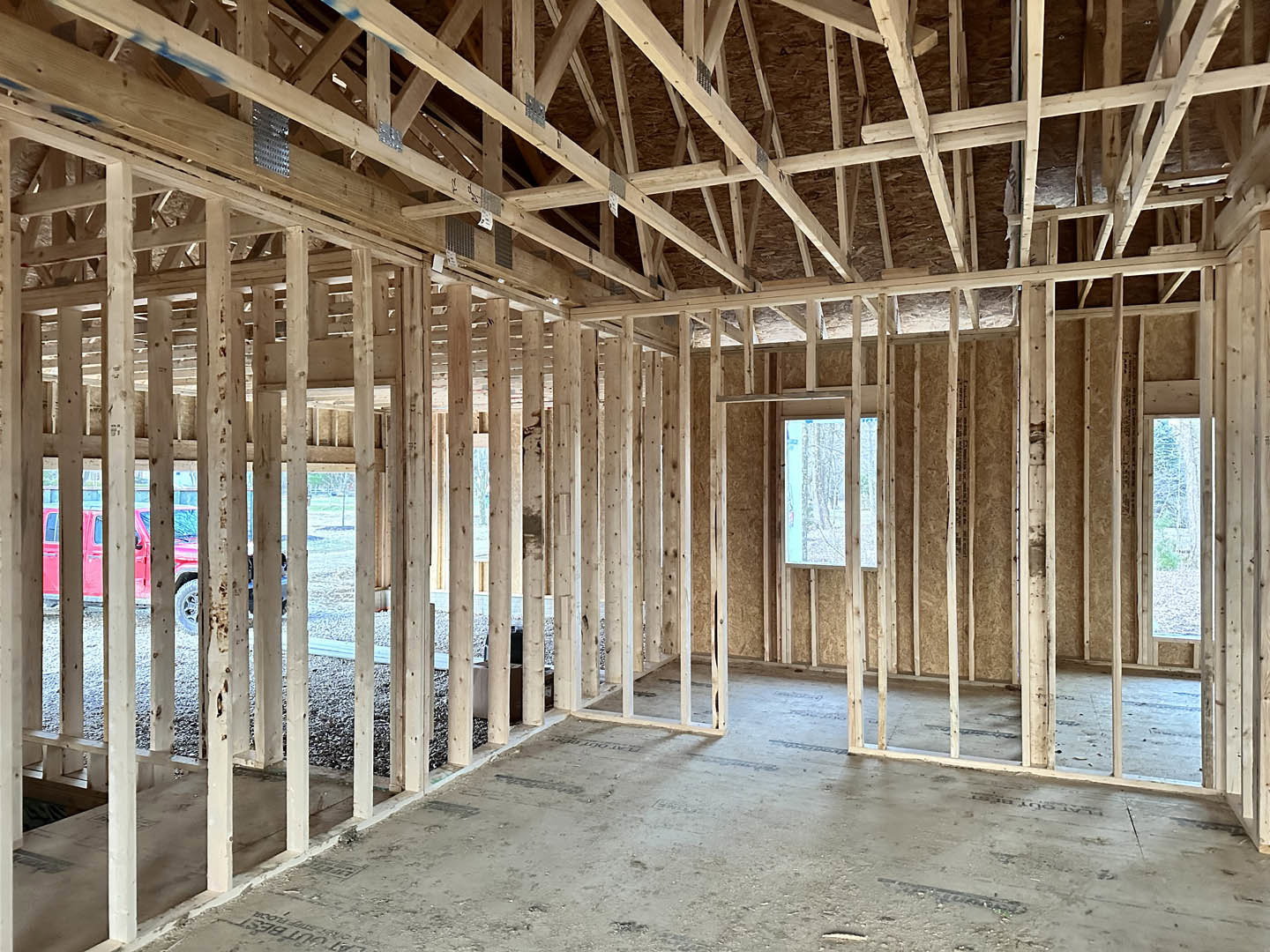 Living room with exposed wood ceiling beams, large window overlooking trees, concrete floor, and white walls