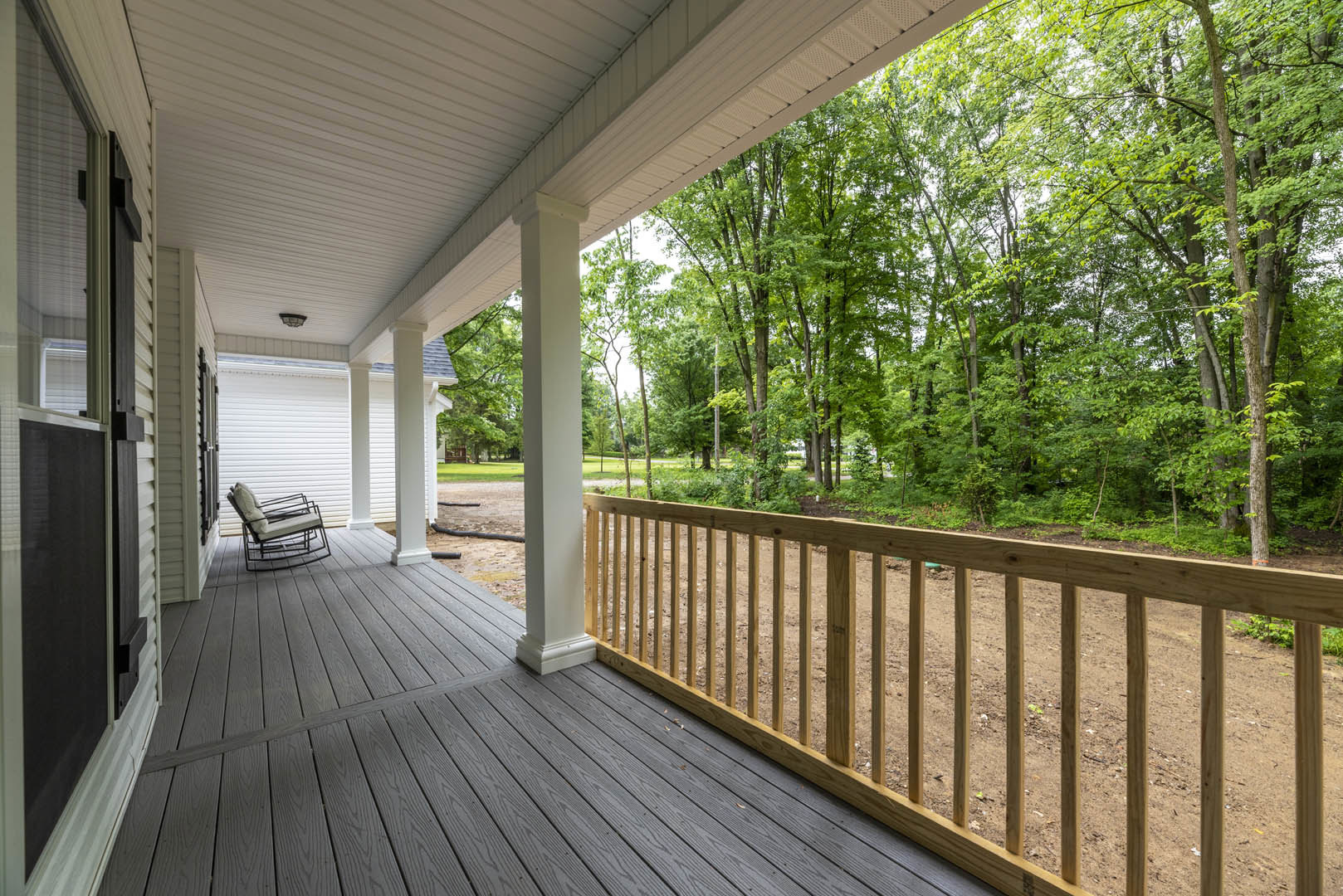 Wooden porch with white pillars, bench with cushion, fenced yard, trees and dirt path, close-up window, shaded outdoor deck