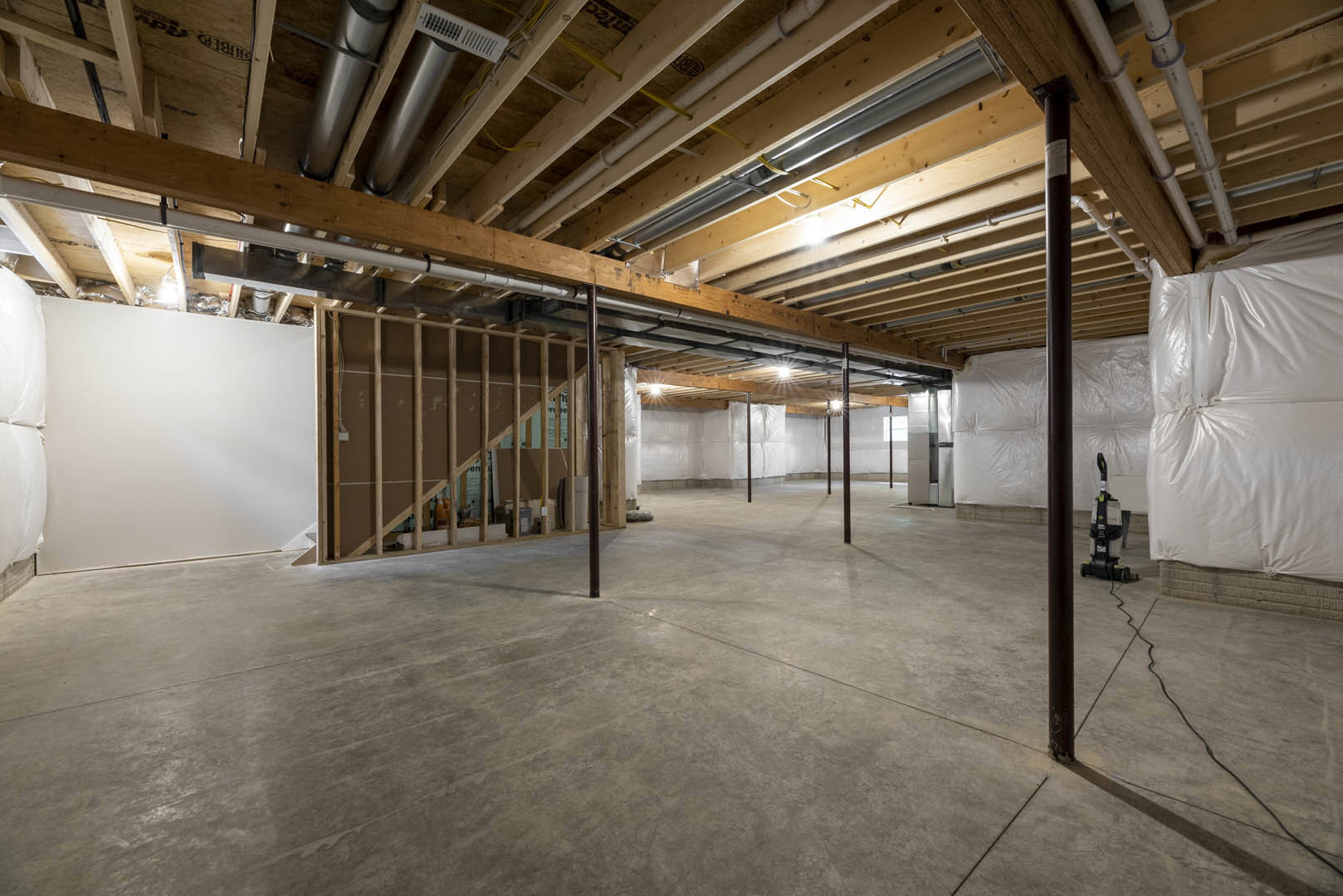 Concrete floor and wooden ceiling in a modern room, white couch positioned near structural pillars, wall with an opening, sheets of paper placed side by side on the floor, black