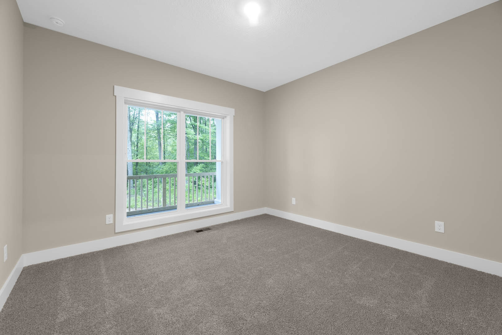 Carpeted room with large window, white ceiling light, and white railing; window overlooks deck and trees