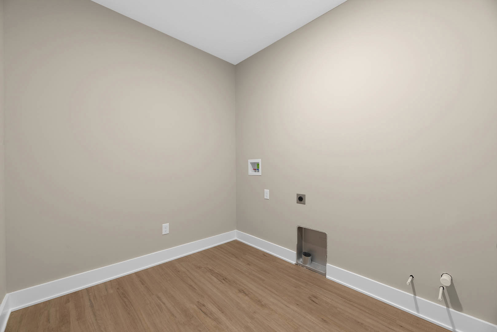 Wood flooring with white baseboards, white plaster wall, and white ceiling in a residential interior.