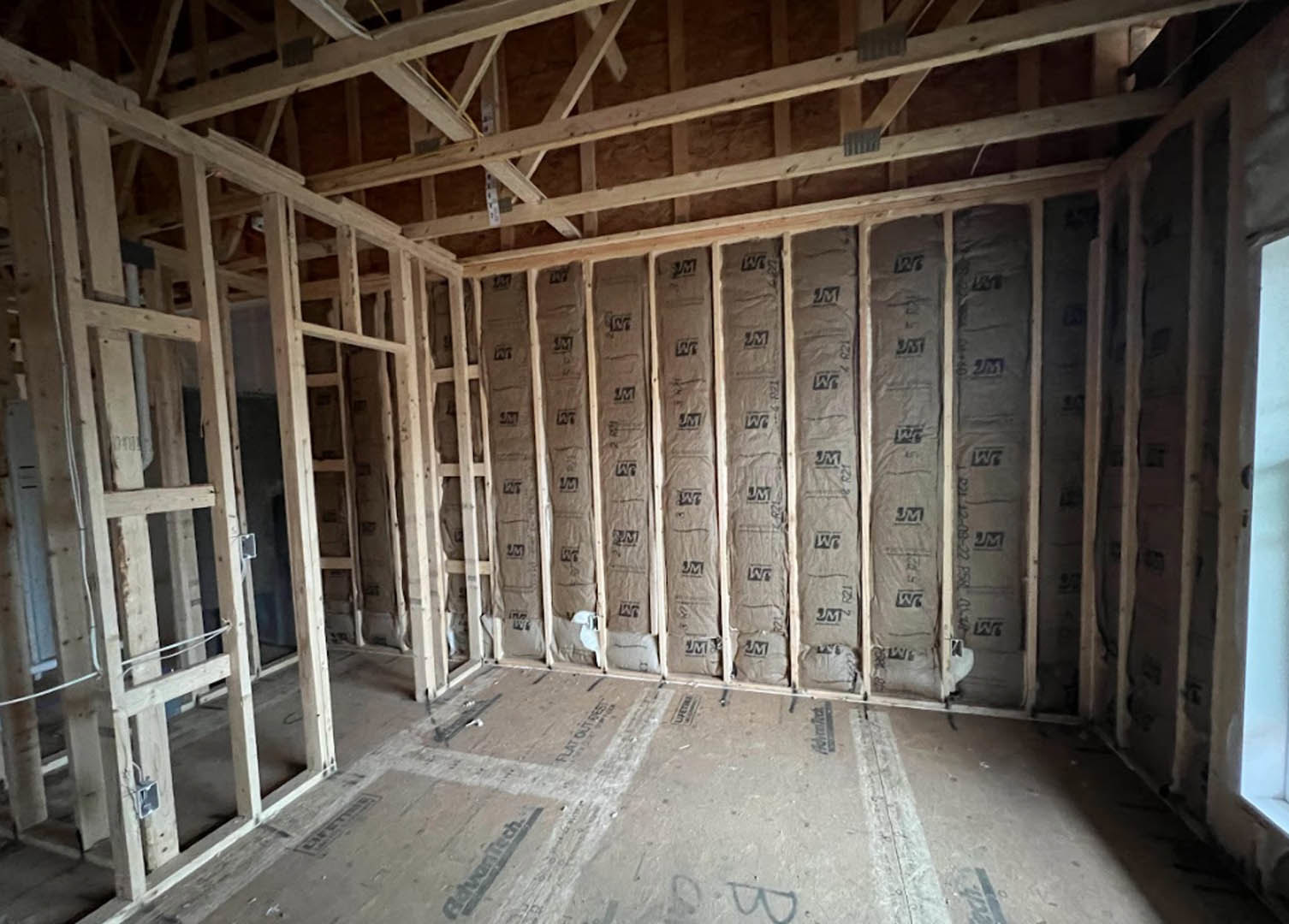 Living room with exposed wood ceiling beams, accent wall covered in paper bags, hardwood flooring, and natural light