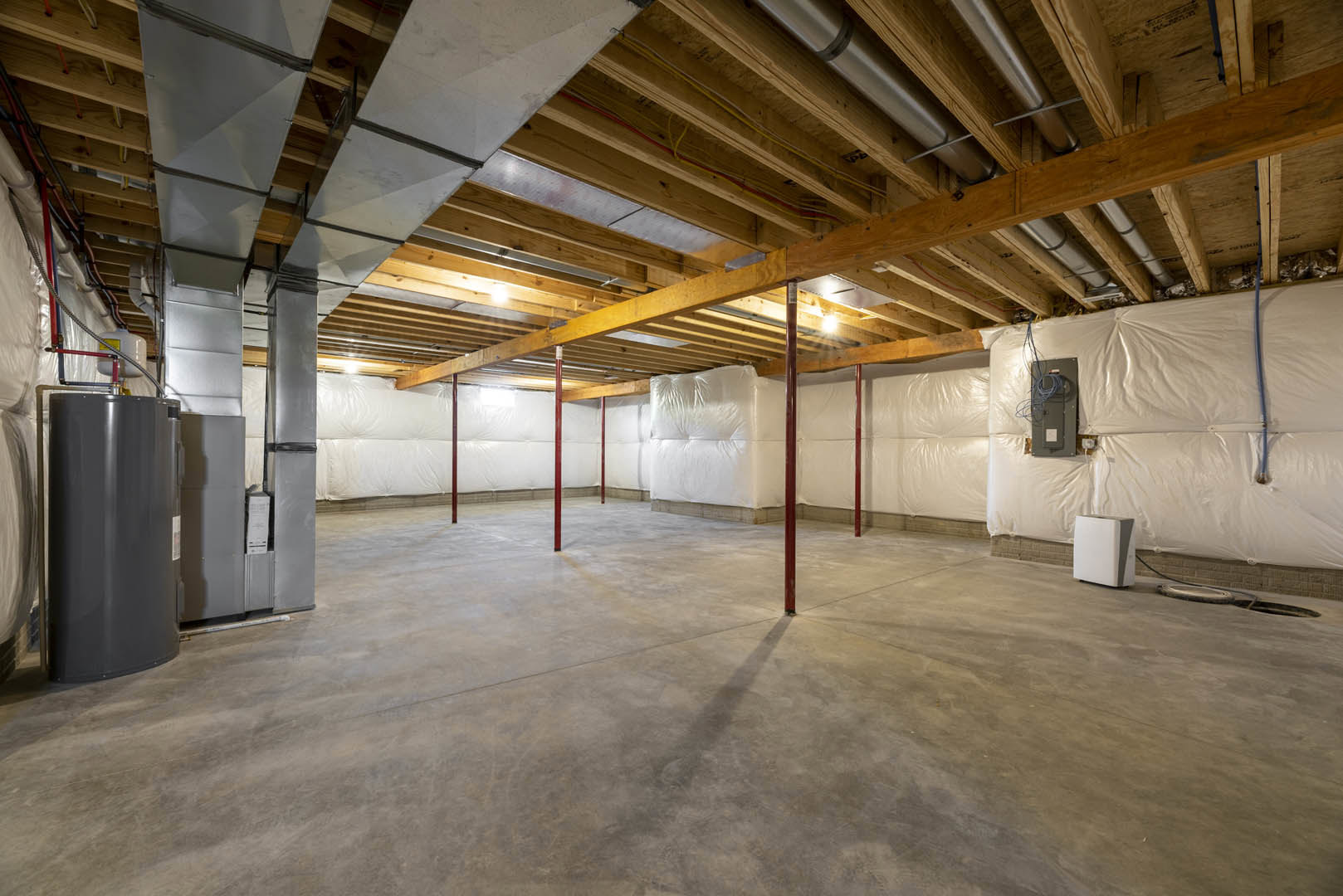 Spacious room featuring white walls, exposed wooden ceiling beams, light wood flooring, and minimal furnishings