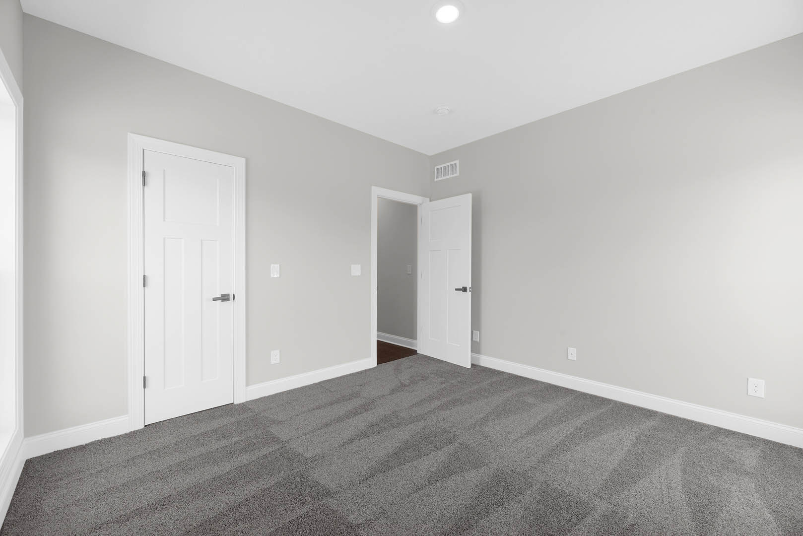 White paneled doors with silver and black handles, grey carpet flooring, white plaster walls, circular ceiling light fixture
