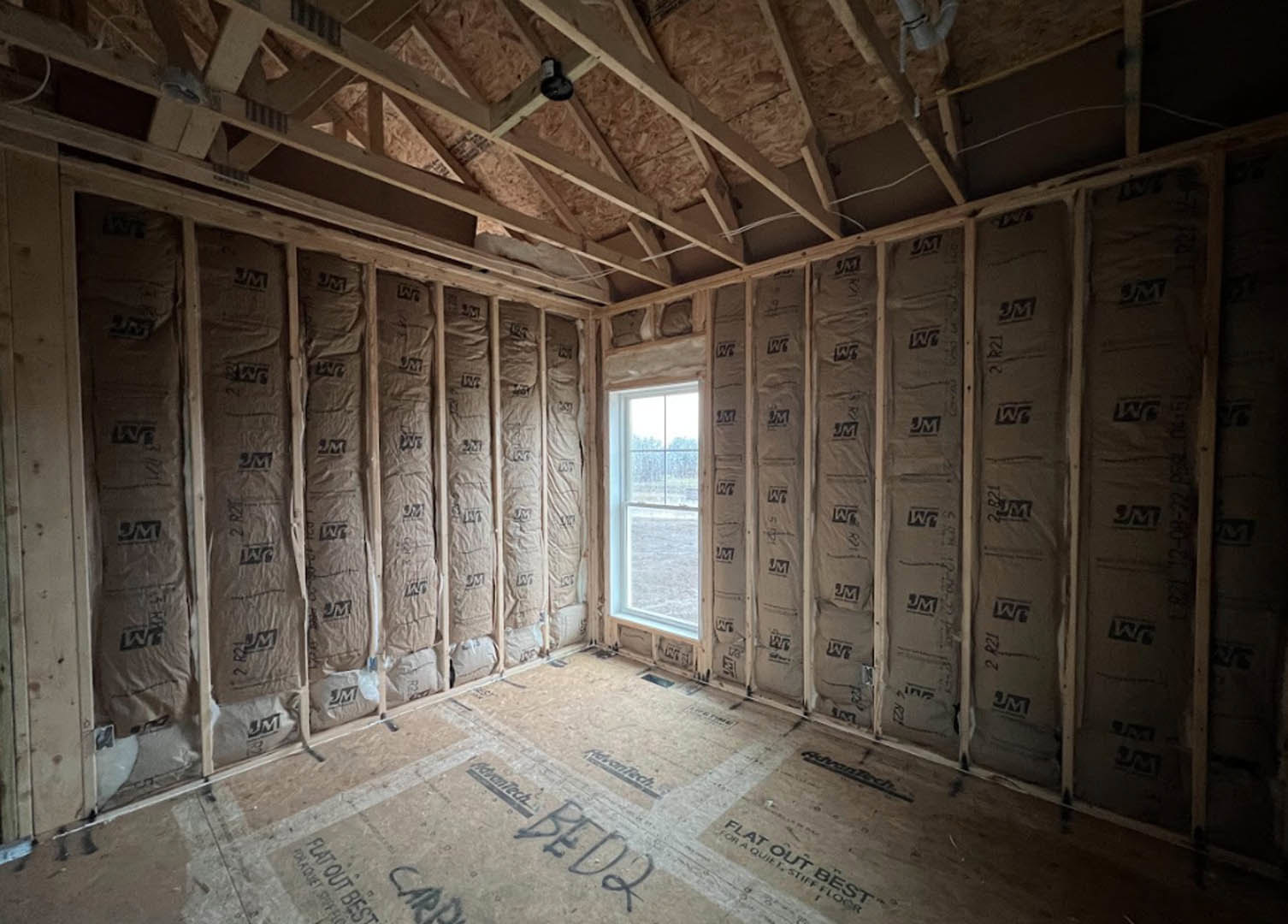 Modern room featuring two large windows with snowy field views, exposed wood beams, light plank flooring, white walls, and a concrete accent surface.