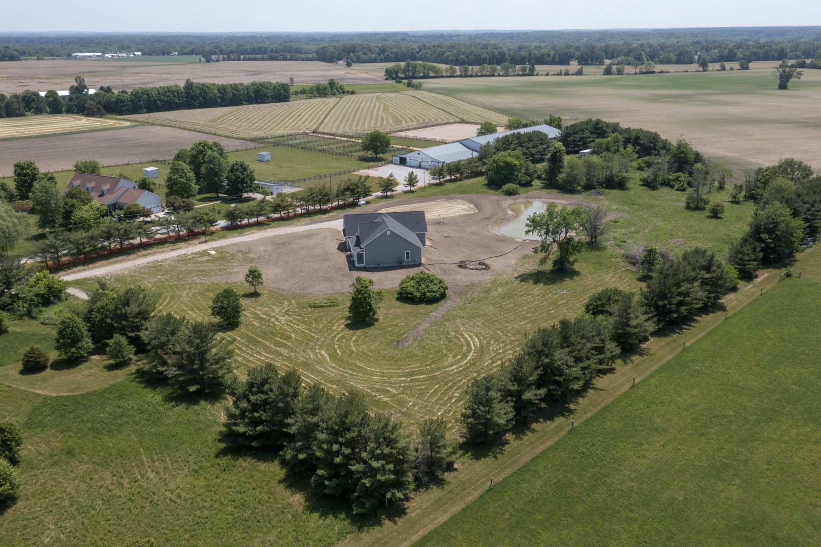 Modern custom home with gray roof and white siding, surrounded by green grass and scattered trees, set on a spacious open field under a clear sky