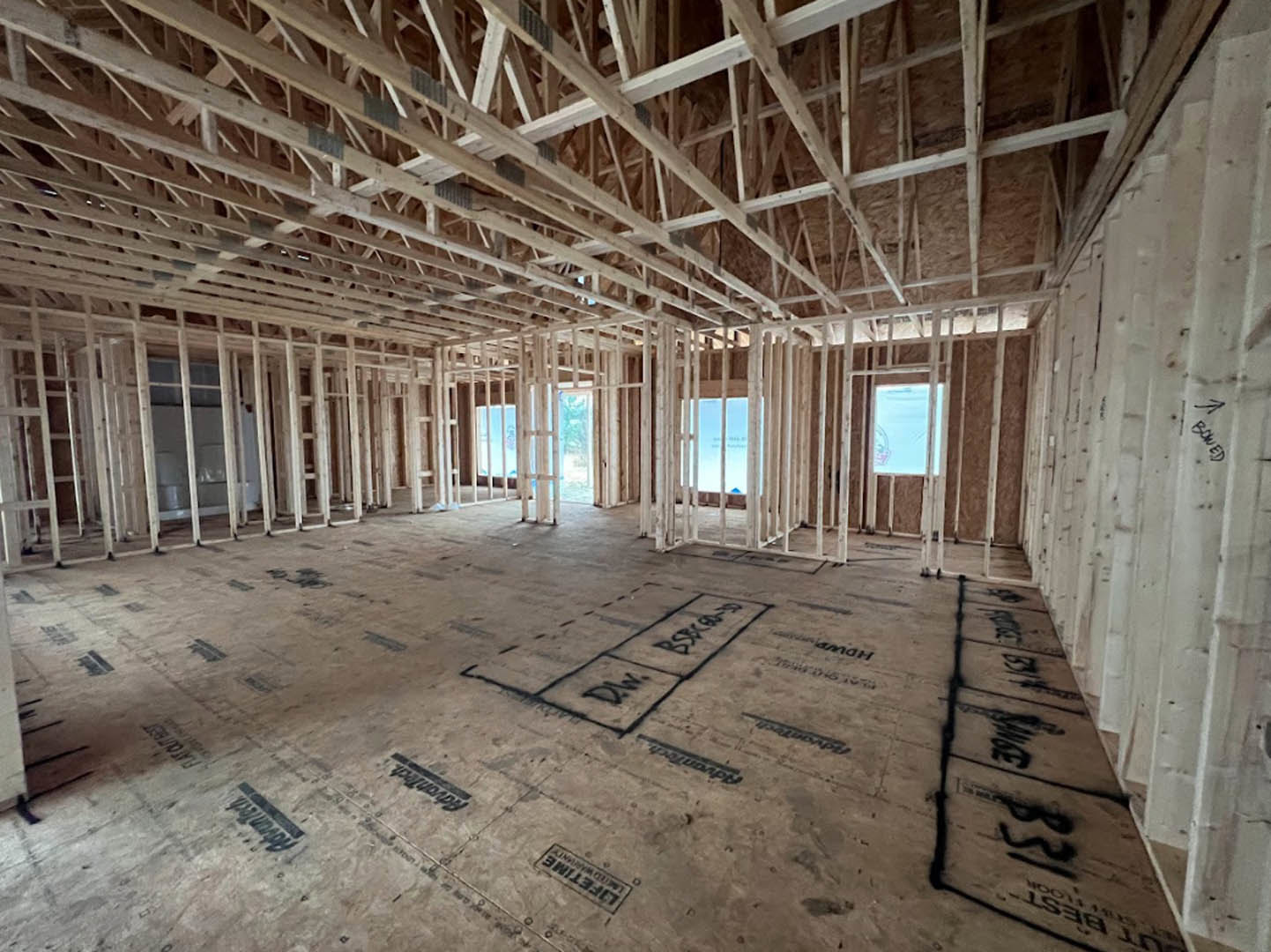 Spacious room with exposed wood ceiling beams, unfinished gray floor marked with black writing, large window letting in natural light