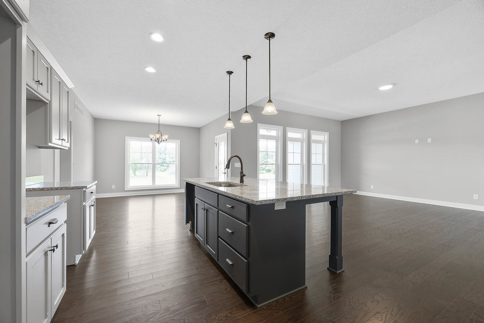Open kitchen with wide wood plank flooring, large central island featuring built-in sink, white cabinetry, stone countertops, glass pendant light fixtures, stainless steel