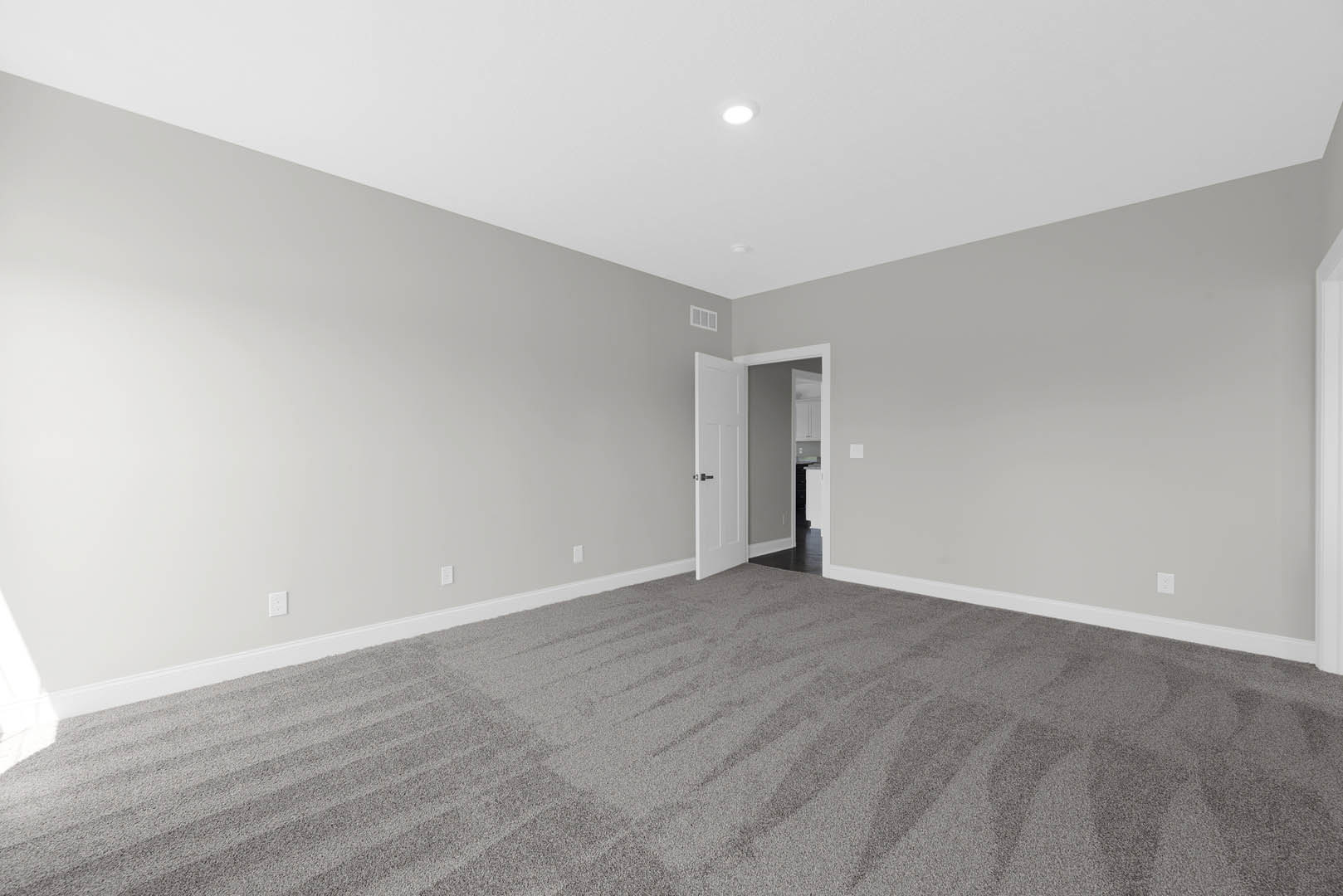 White paneled door with matte black handle open onto carpeted room, white walls and ceiling with recessed light, soft shadow cast along baseboard.