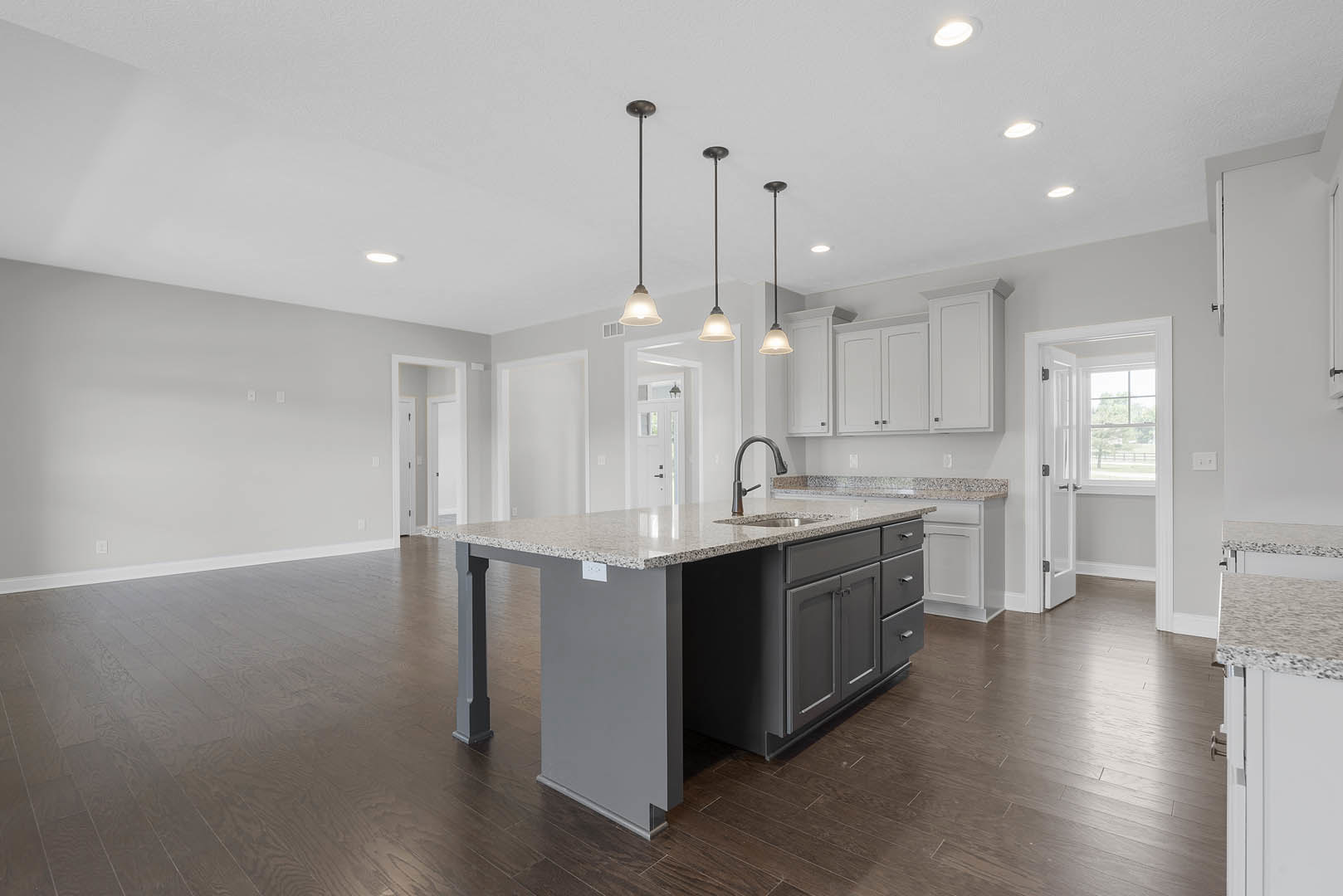 Spacious kitchen featuring a large central island with built-in sink, white cabinetry, light countertops, stainless steel faucet, and a white door with window in the background.