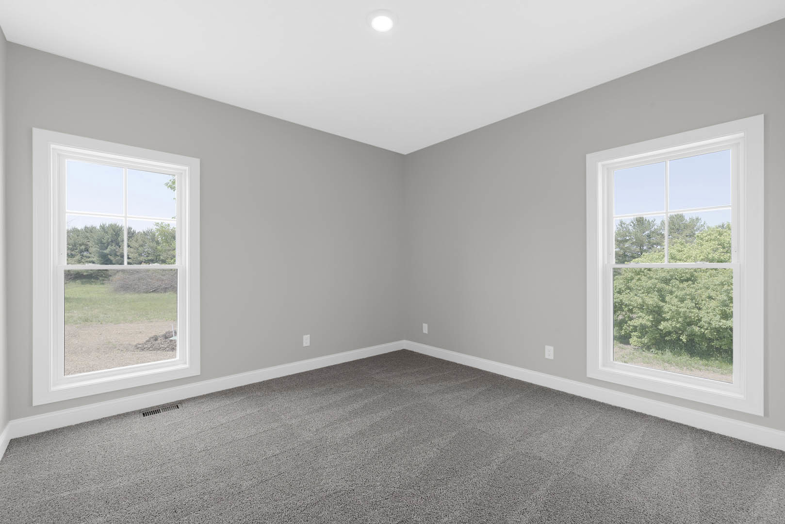 Bright room with large windows overlooking grass and trees, grey carpet flooring, white walls with crown molding, recessed ceiling light