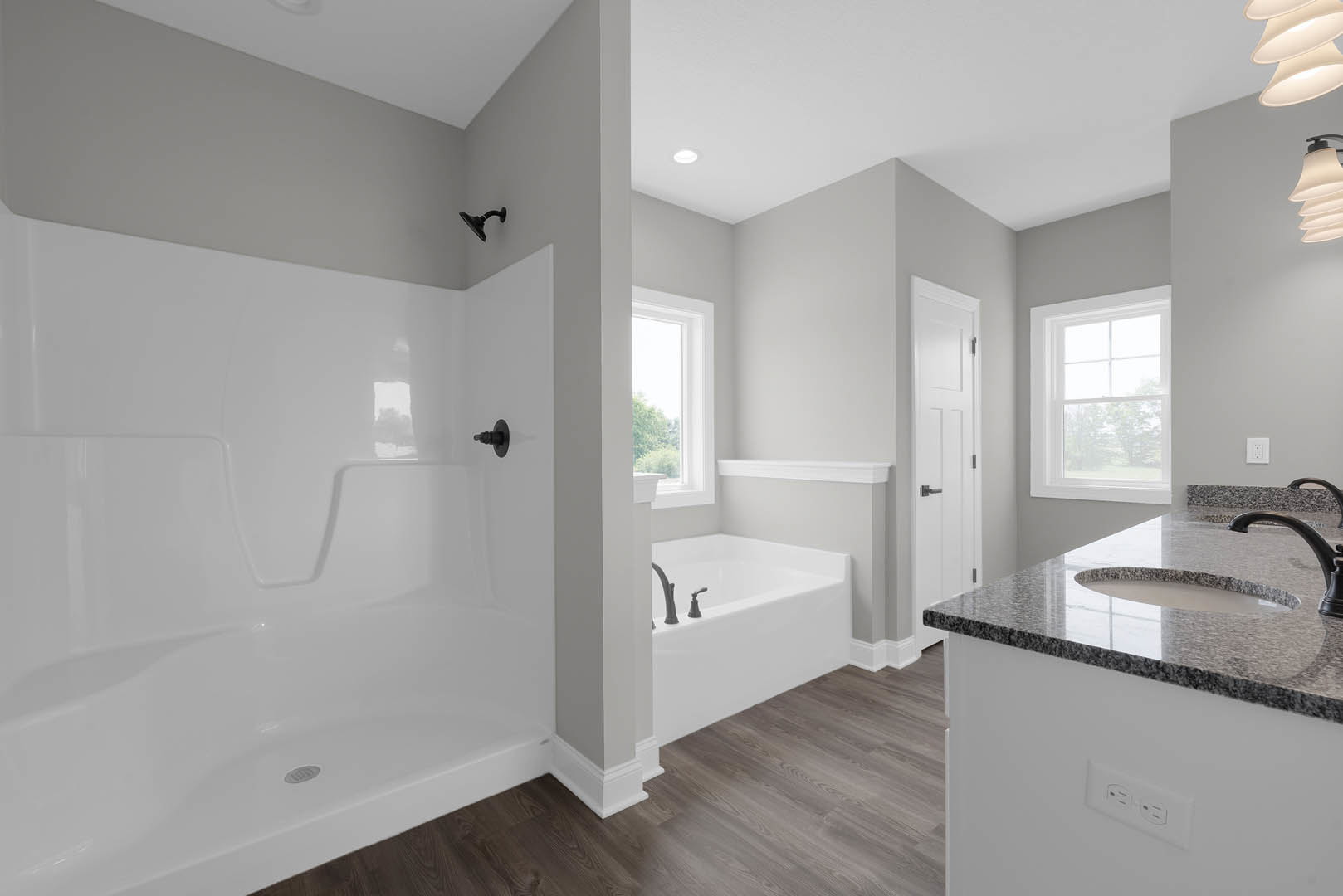 Bathroom with white tub and shower, white tile walls, window with white frame, black wall-mounted light fixture, white door with black handle, black round metal object on wall.