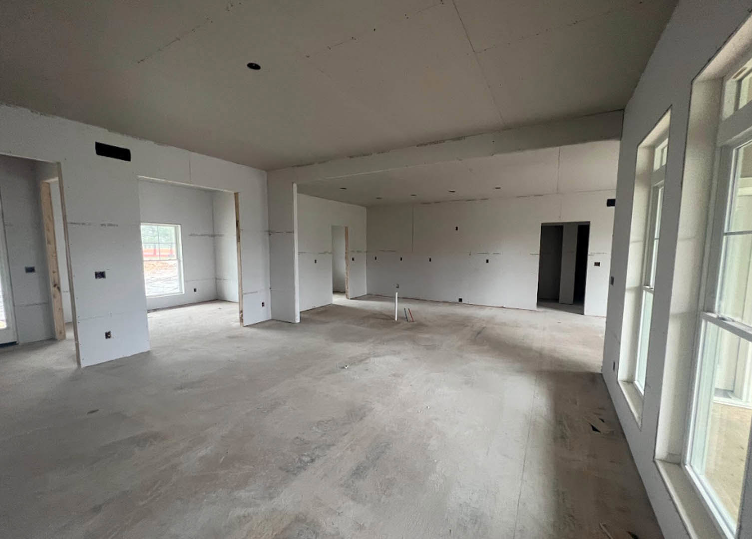 Concrete floor and white walls with bold black and white striped accent wall, large windows offering outdoor view, minimalist interior finishes.