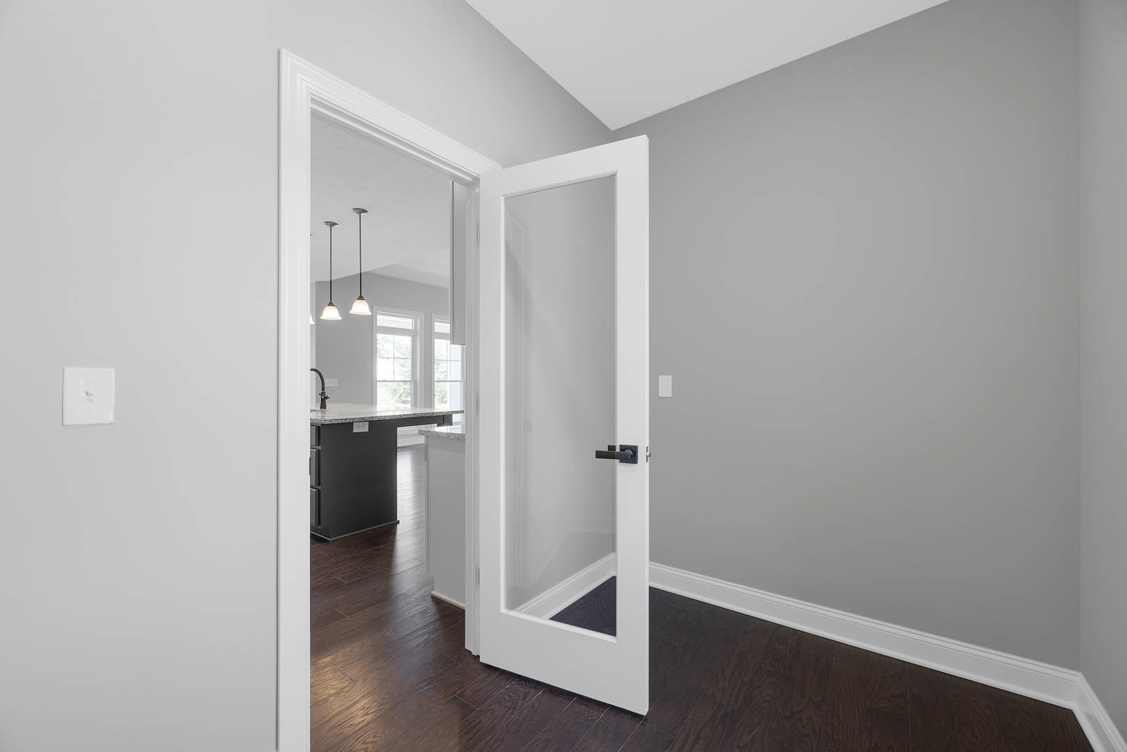 White paneled door with black lever handle set in a plaster wall, laminate flooring, nearby white electrical outlet, partial view of kitchen island with sink, black and white