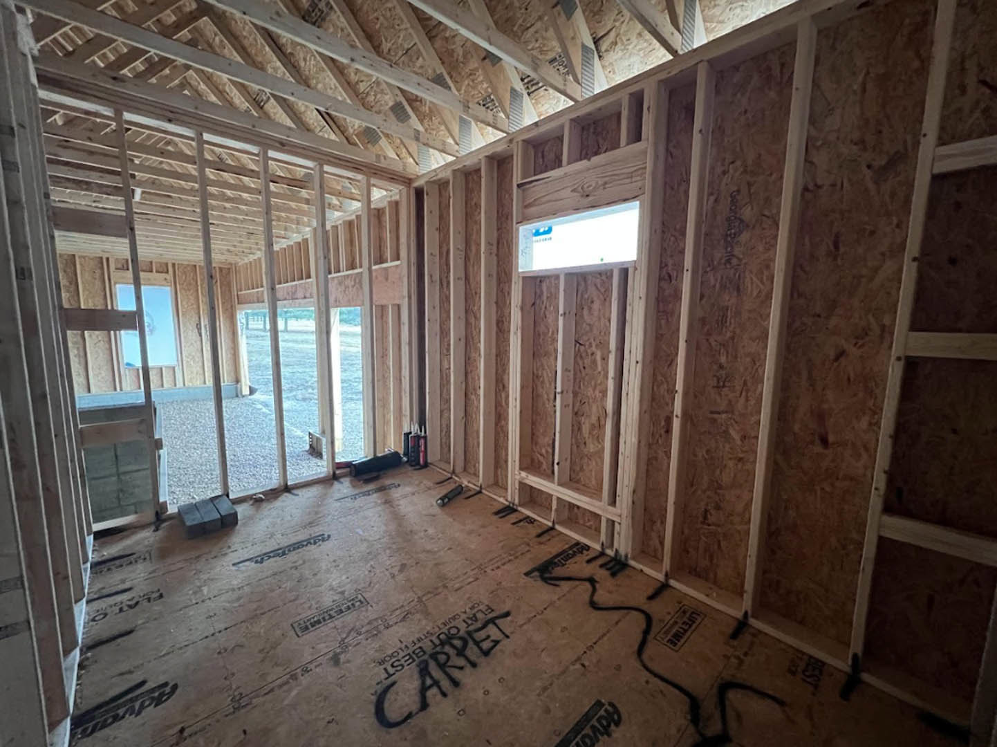 Living room with exposed wood ceiling beams, large window, white plaster walls, and neutral carpet flooring.