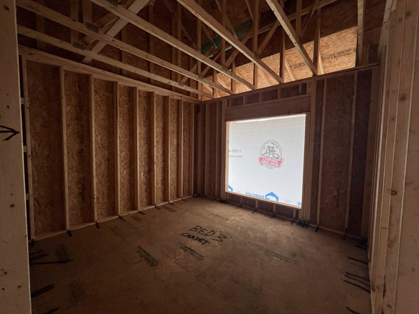 Bedroom with exposed wooden ceiling beams, large window, white walls, and light-colored carpet flooring