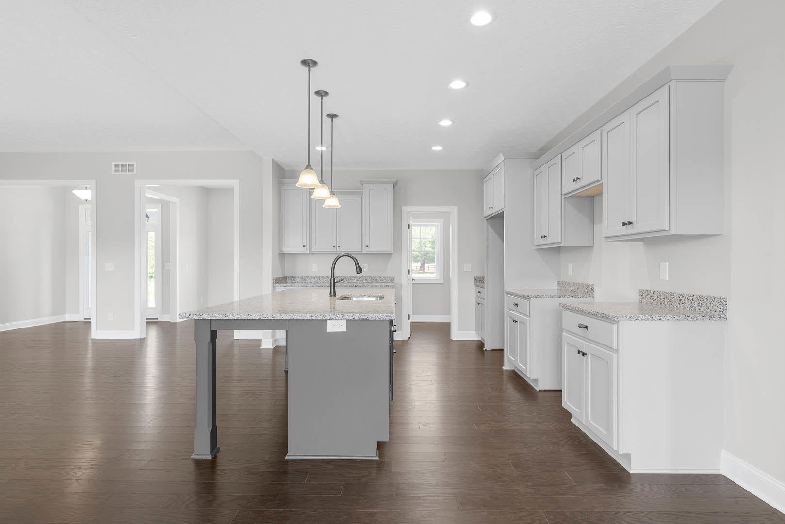 Spacious kitchen featuring a large marble island with built-in sink, white cabinetry, bell-shaped pendant light, white door with window, and a tree visible through the window.