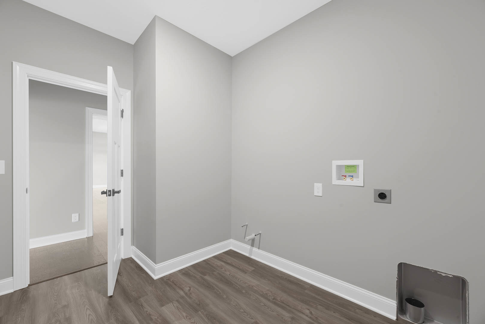 White door with black handles open to a den featuring laminate wood flooring, white plaster walls, black and white electrical outlet, metal tube detail, and silver container on